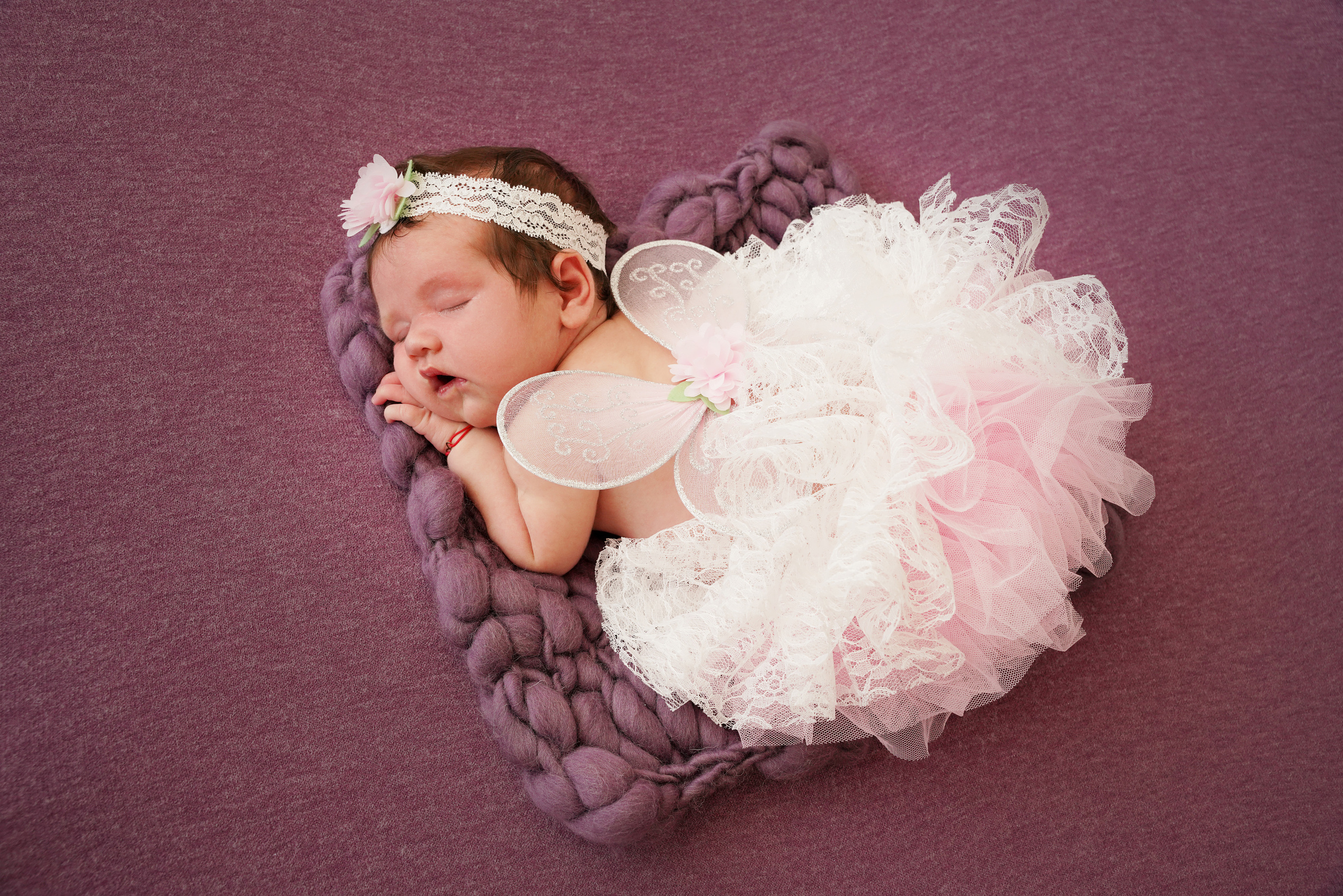auf einer lila Decke liegt ein Neugeborenes  auf dem Bauch in einem üppigen weißen Rock und mit Elfenflügeln auf dem Rücken.