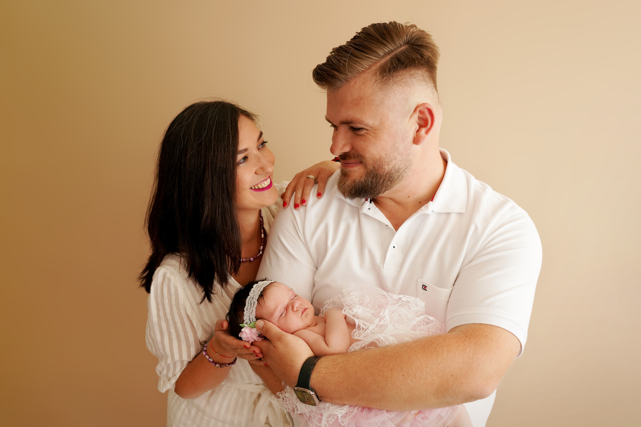 Mama schaut auf Papa und er auf das Neugeborene in seinen Händen