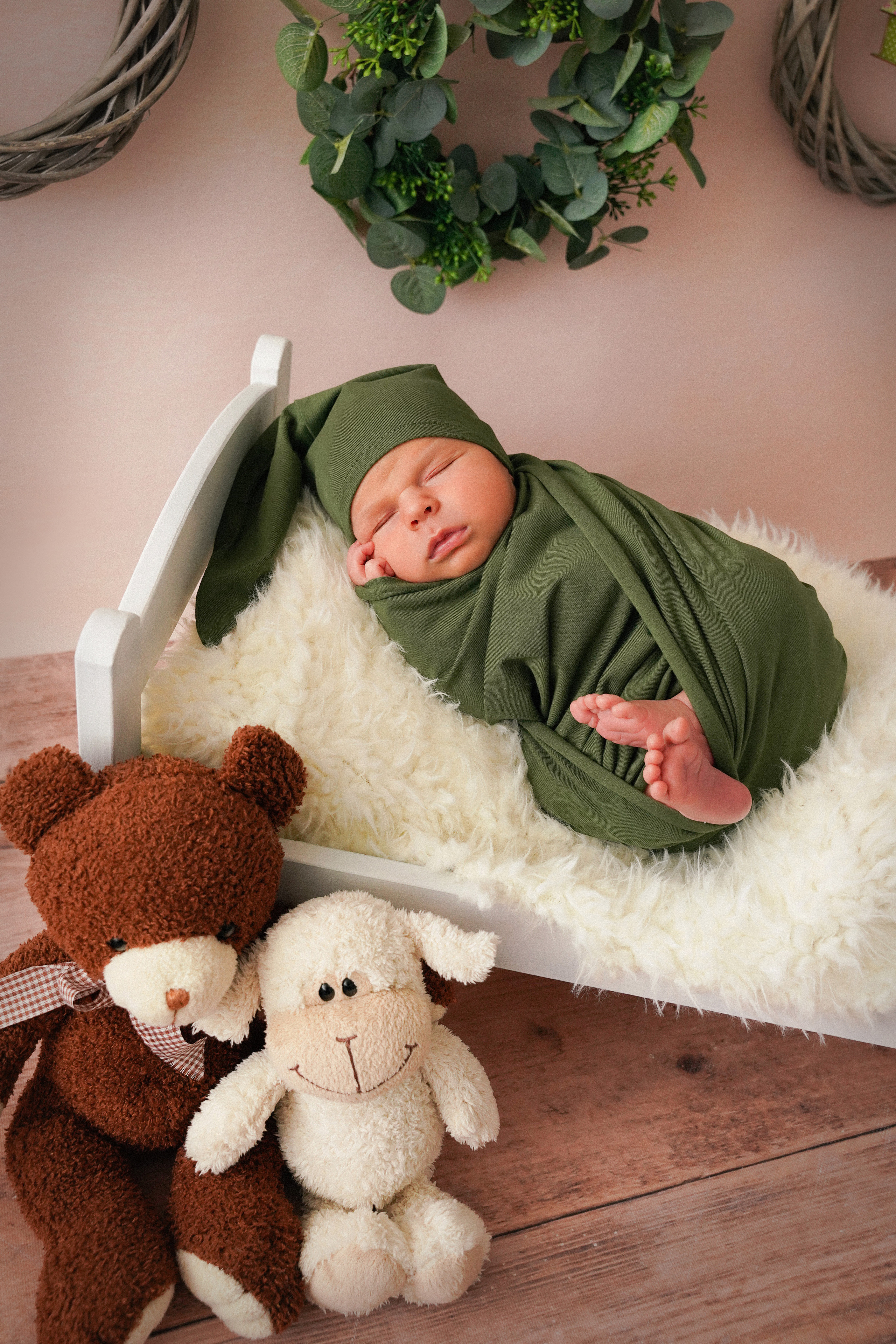 auf dem Bild ein Neugeborenes in einer grünen Mütze auf einer weißen Krippe