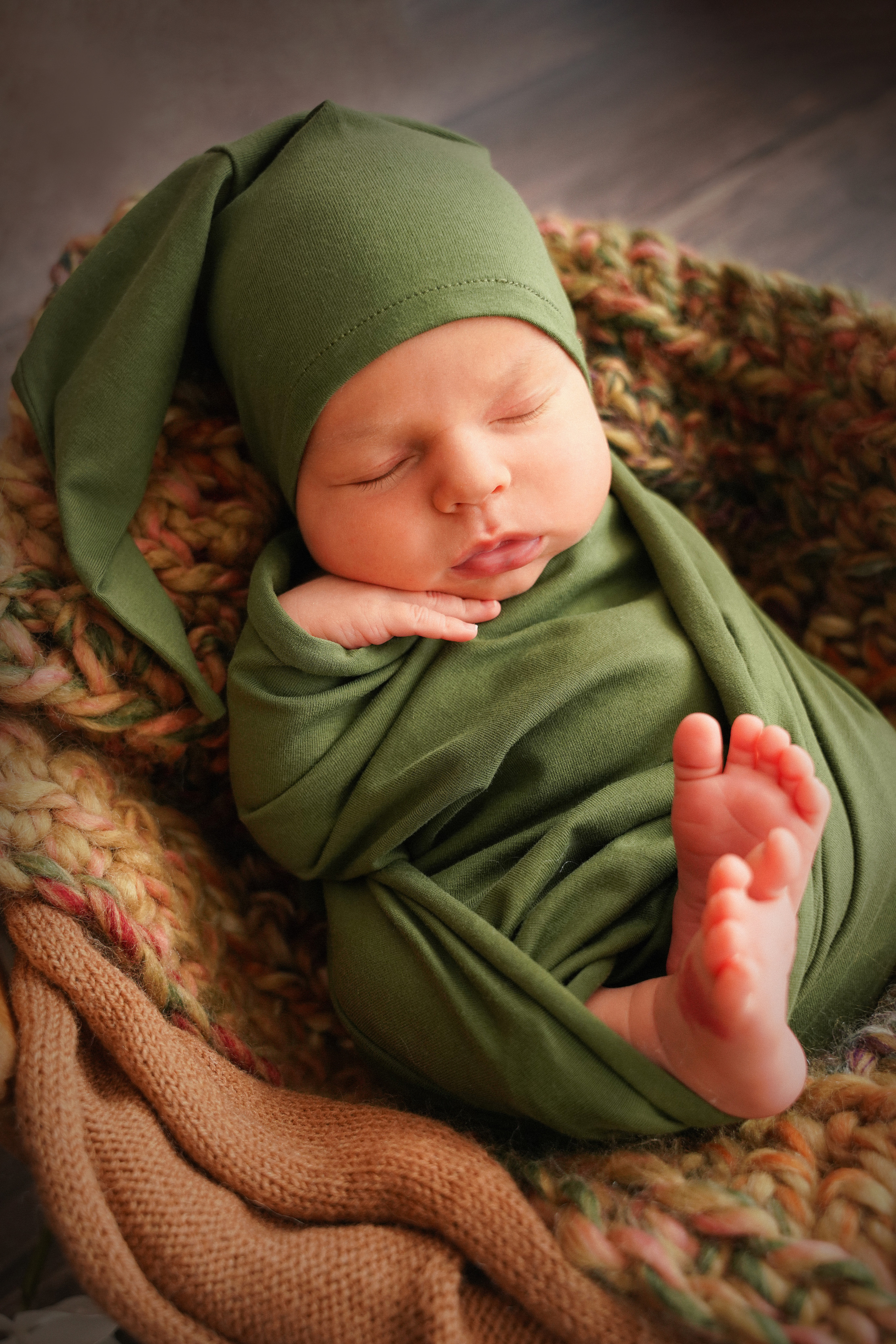 Foto eines Neugeborenen in einer grünen Schlafmütze an der Seite