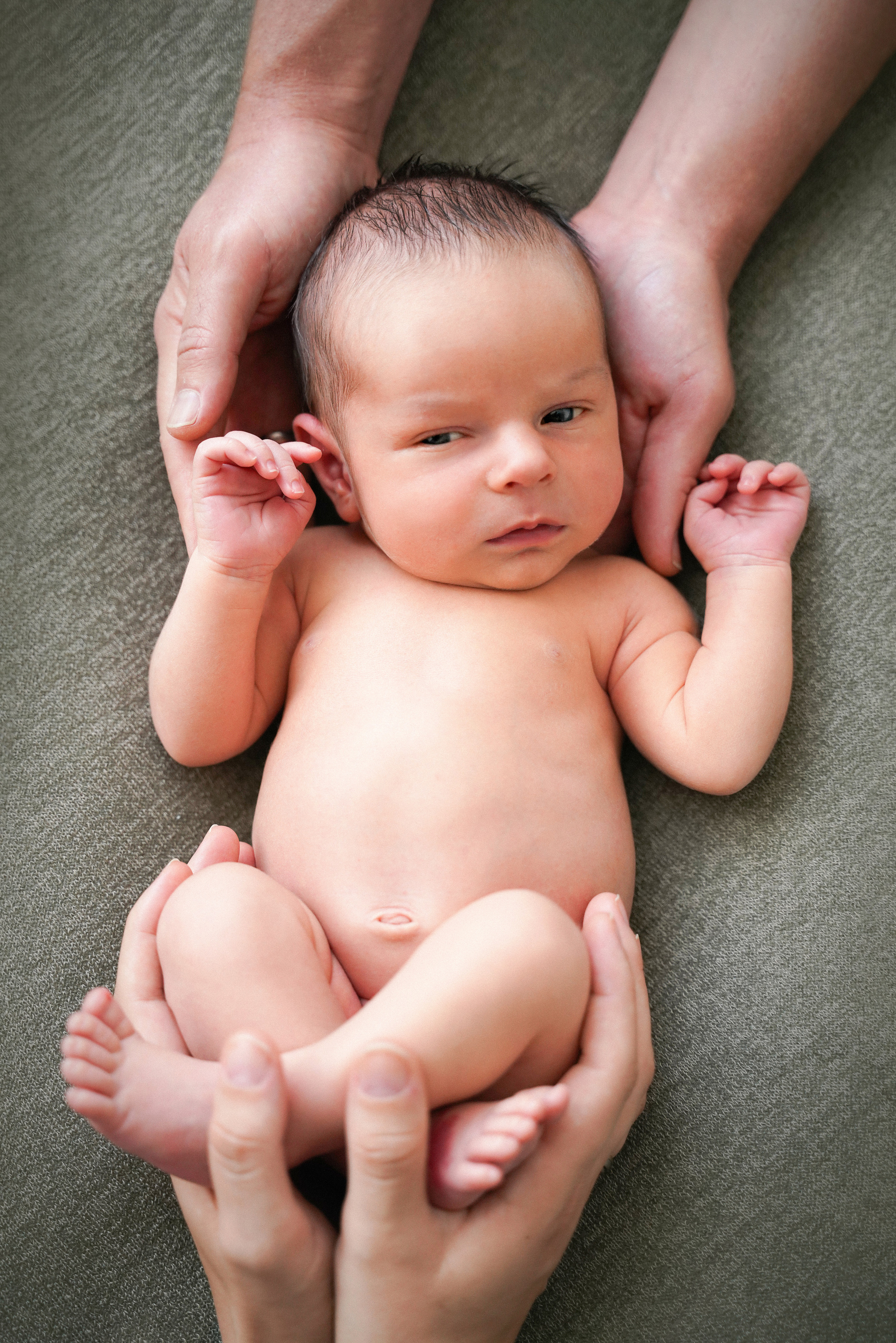 ein nackter neugeborener Junge liegt kopfüber auf papas Händen und seine Füße werden von Mama gehalten