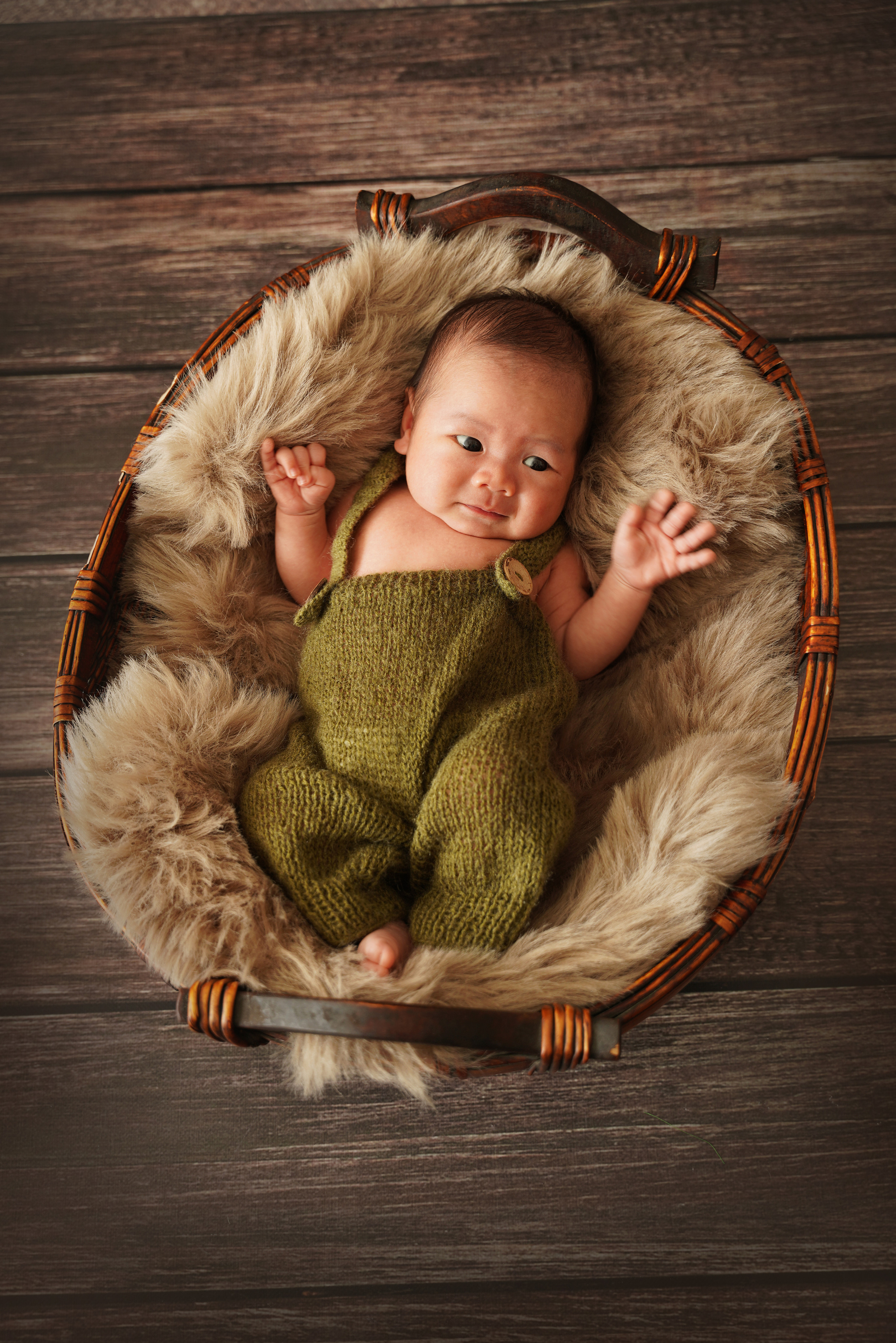 foto eines Neugeborenen Jungen in einem grünen Overall auf einer Pelzdecke
