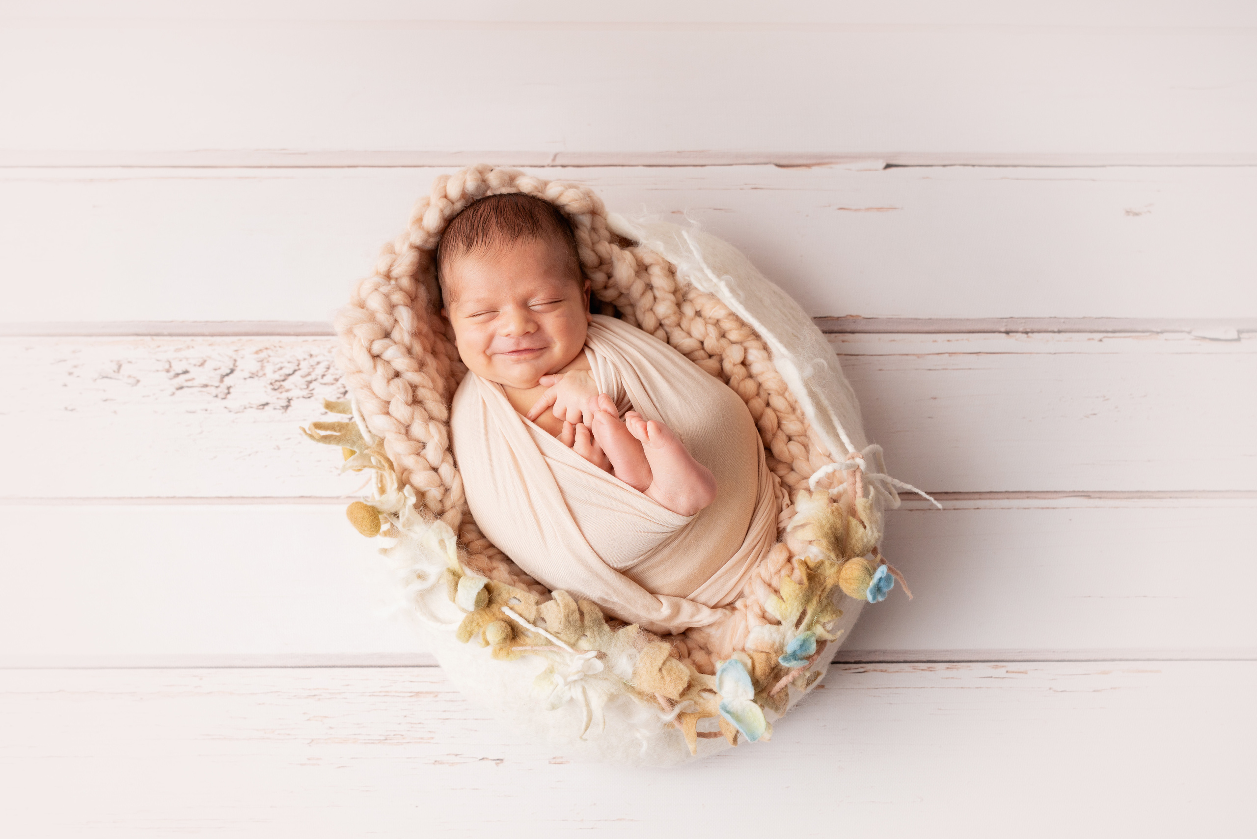 Ein Neugeborenes liegt in einem Nest auf hellem Hintergrund und lächelt