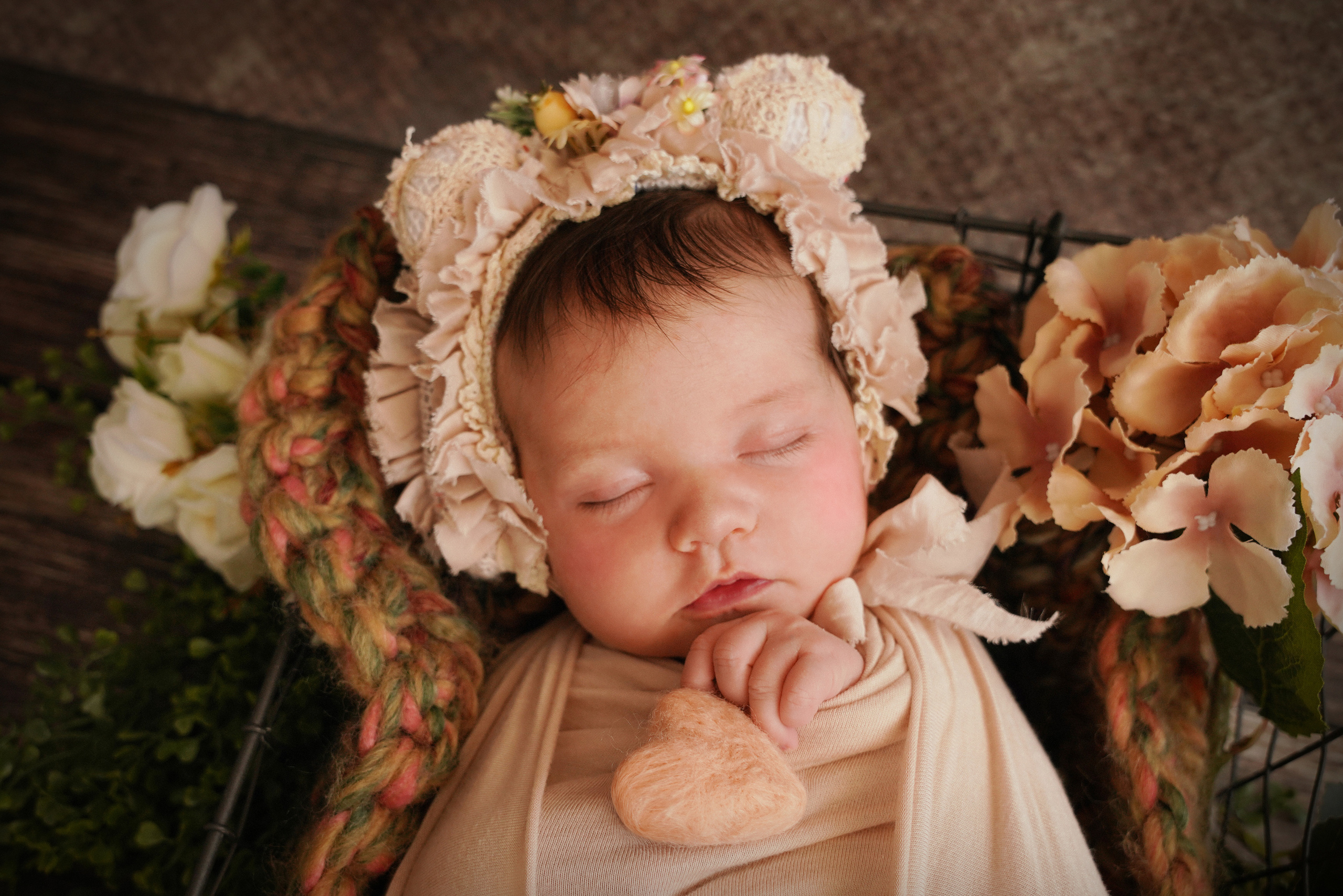 auf dem Baby eine Mütze mit Ohren und Blumen und ein pfirsichfarbenes Herz in der Hand