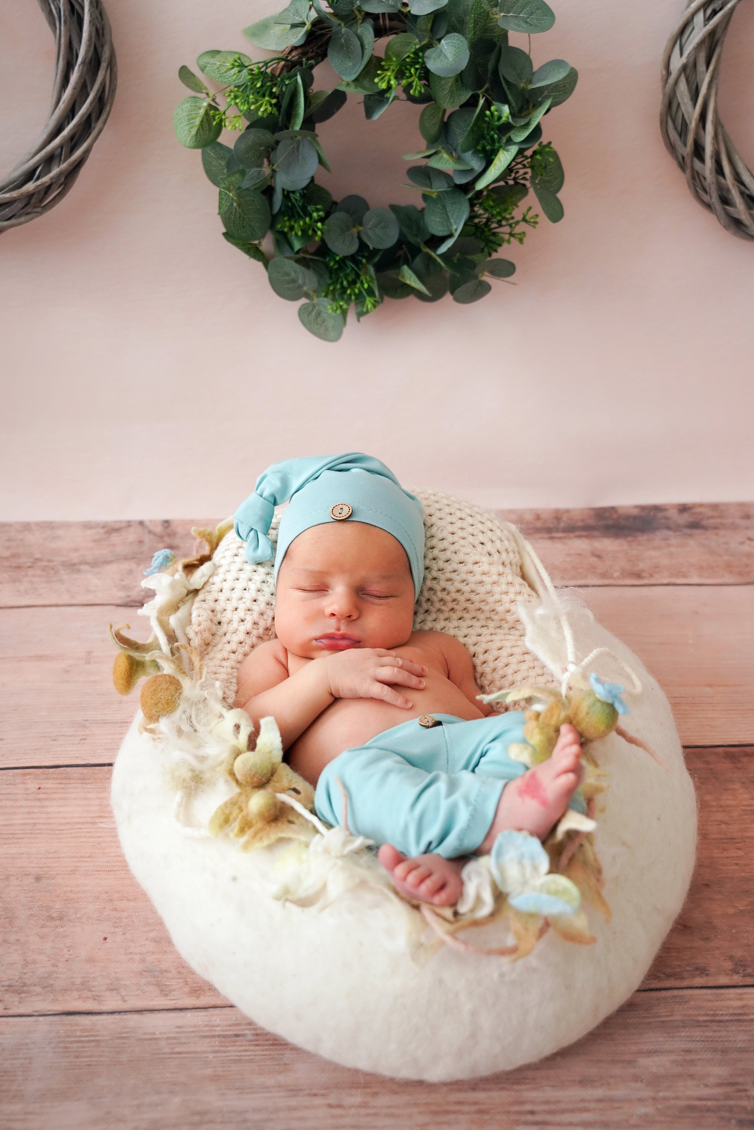 das Baby liegt in einer blauen Hose und einer Schlaffmütze in einem weißen Nest aus Wolle.