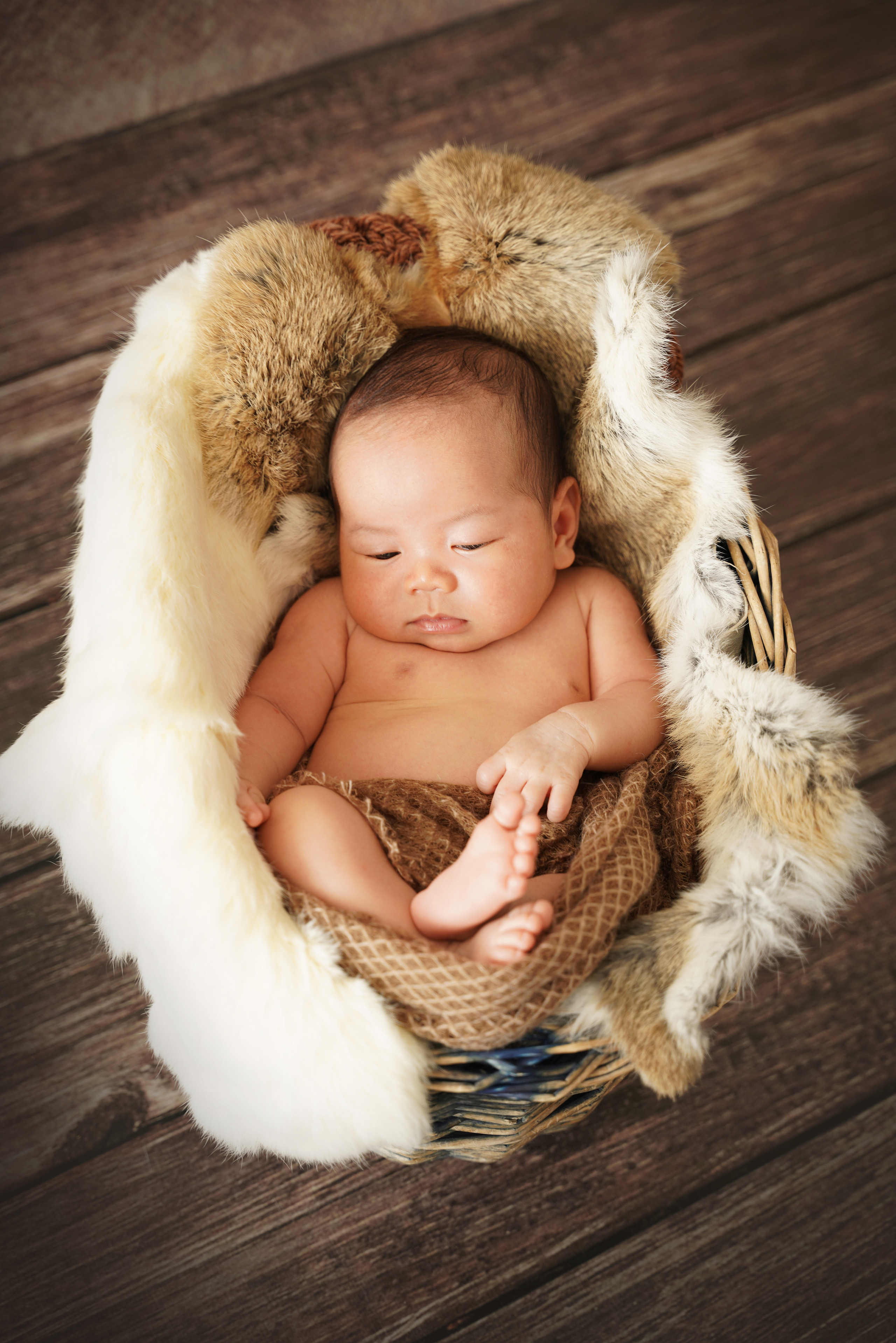 Junge schläft liegend auf Fell in einem Korb für Neugeborene