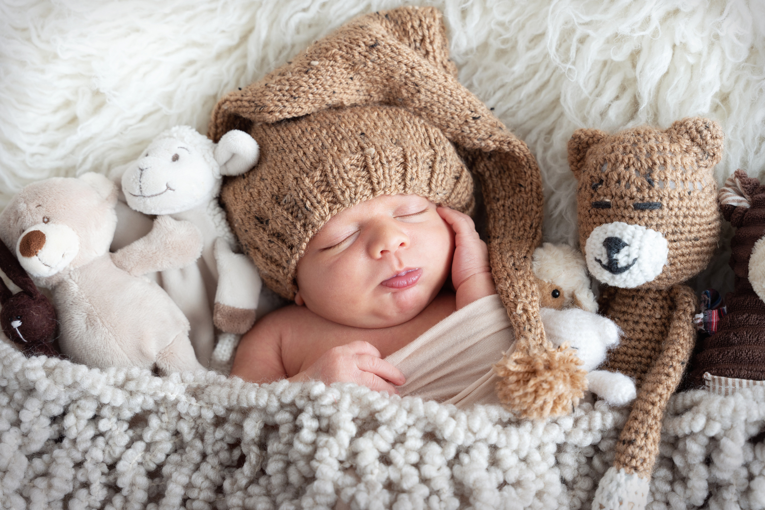 Das Baby schläft zwischen Plüschtieren und stützt seine Wange mit seinem Boot