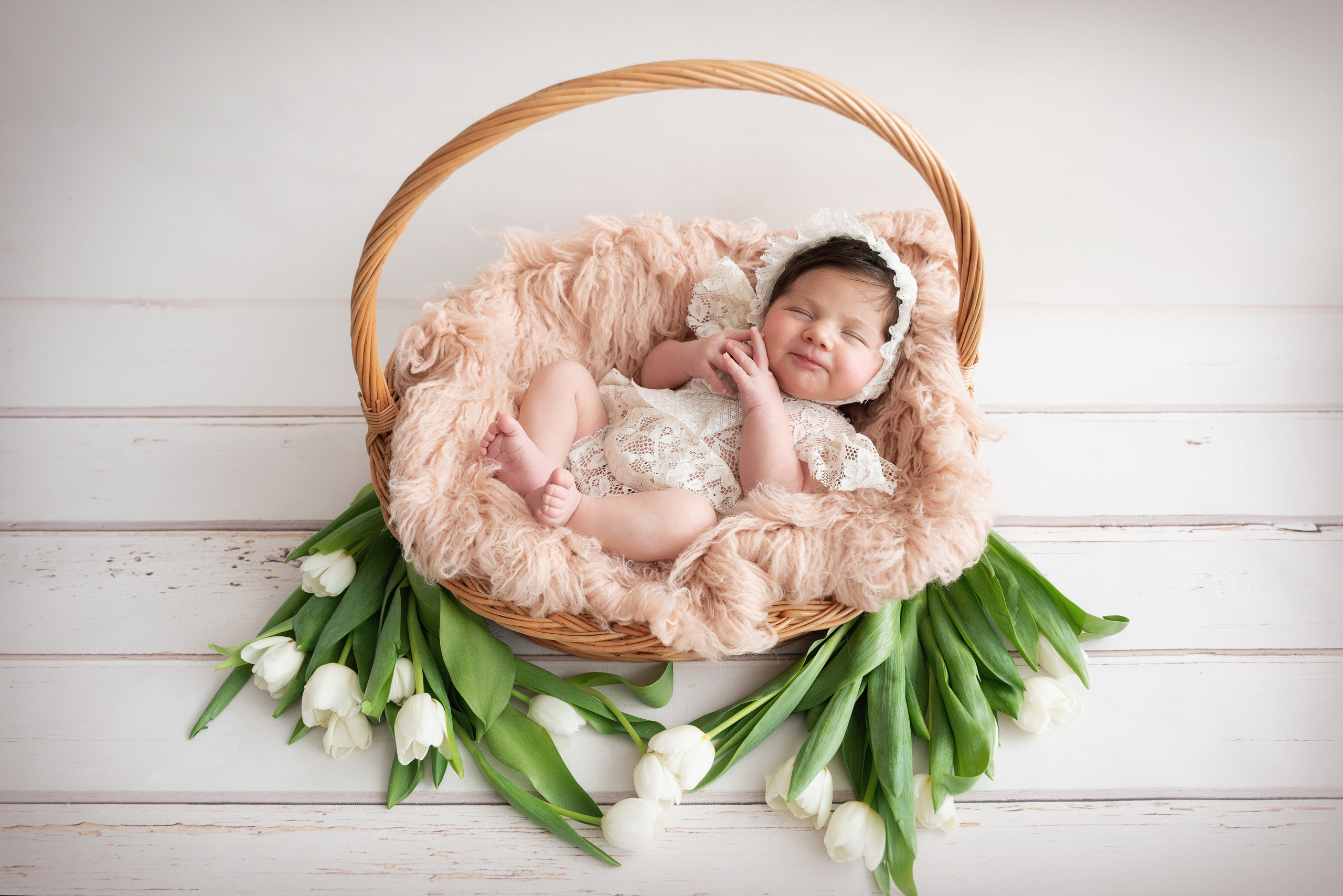 das Baby liegt in einem Korb mit einem Griff und weiße Tulpen liegen darunter