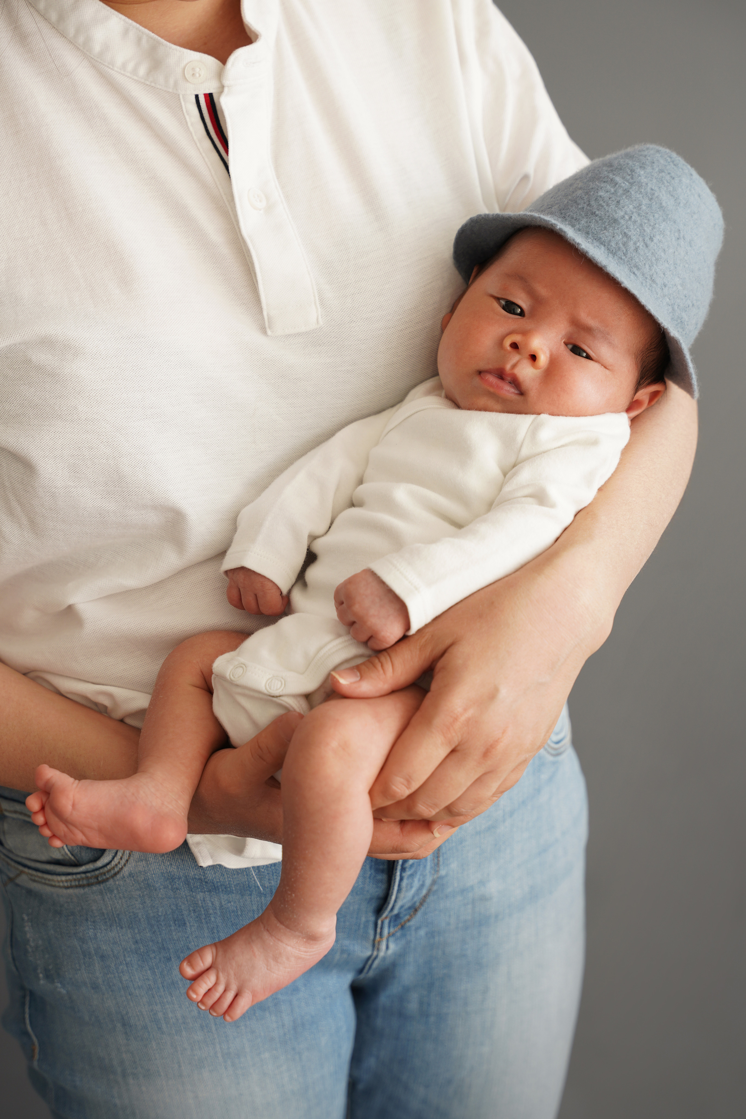 ein Neugeborenes in einem blauen Hut und einem weißen Body schläft auf den Armen seiner Mutter