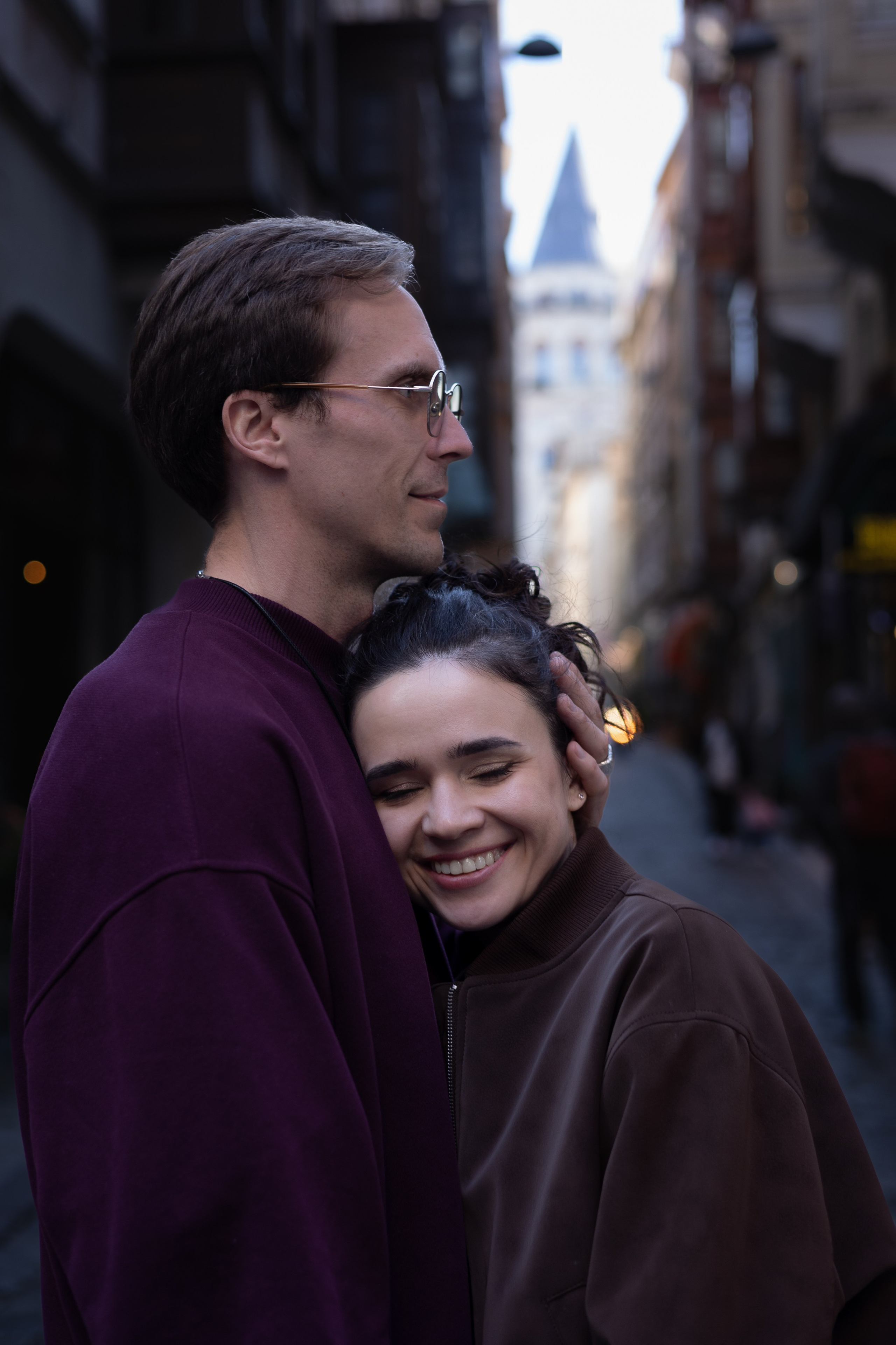 Пара обнимается на узкой городской улице в Стамбуле, на заднем плане видна Галатская башня