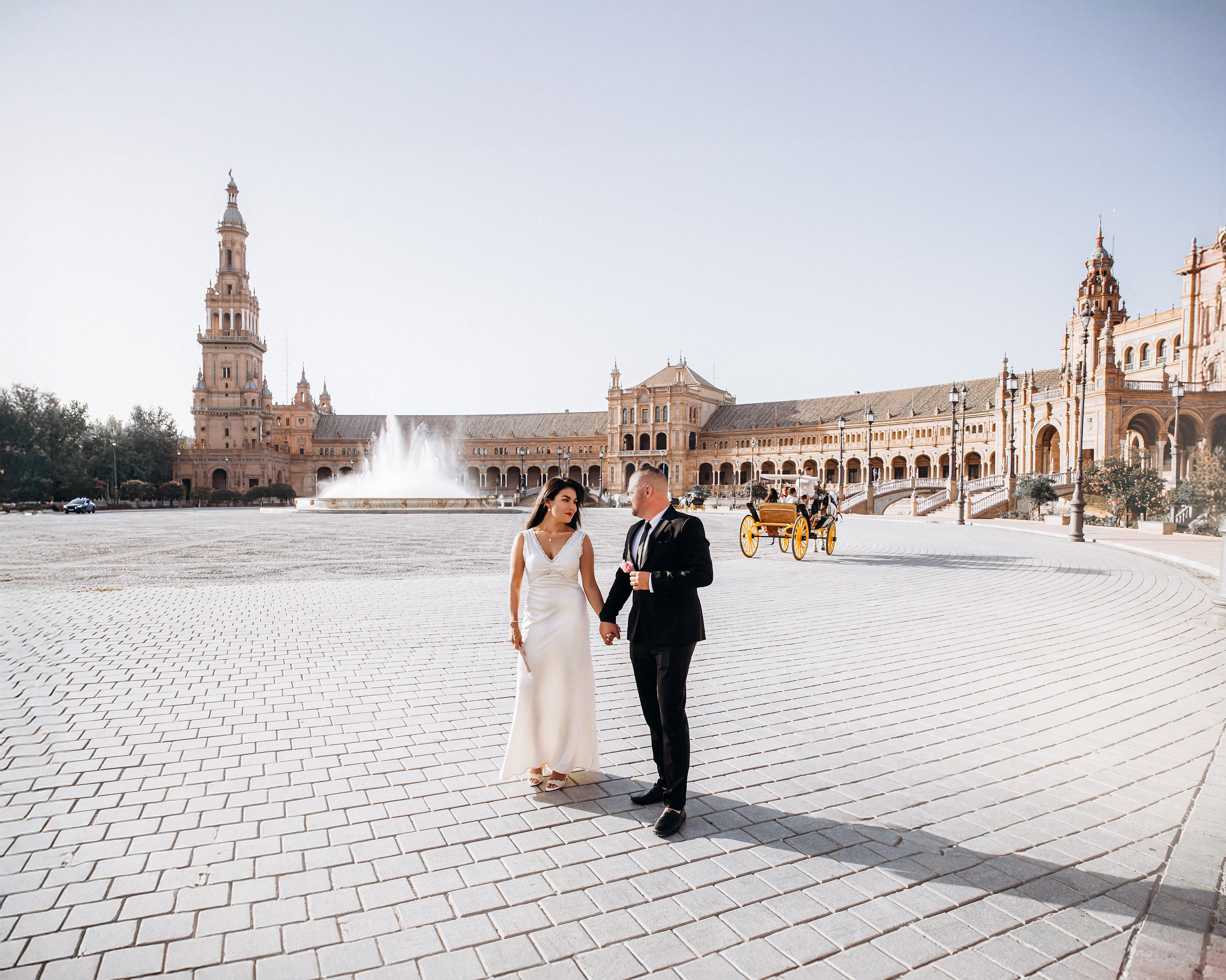Elegant wedding couple walking hand in hand in front of the iconic fountain and grand architecture of Plaza de España in Sevilla, Spain — a perfect setting for romantic and cinematic destination wedding photoshoots in Seville and southern Spain.