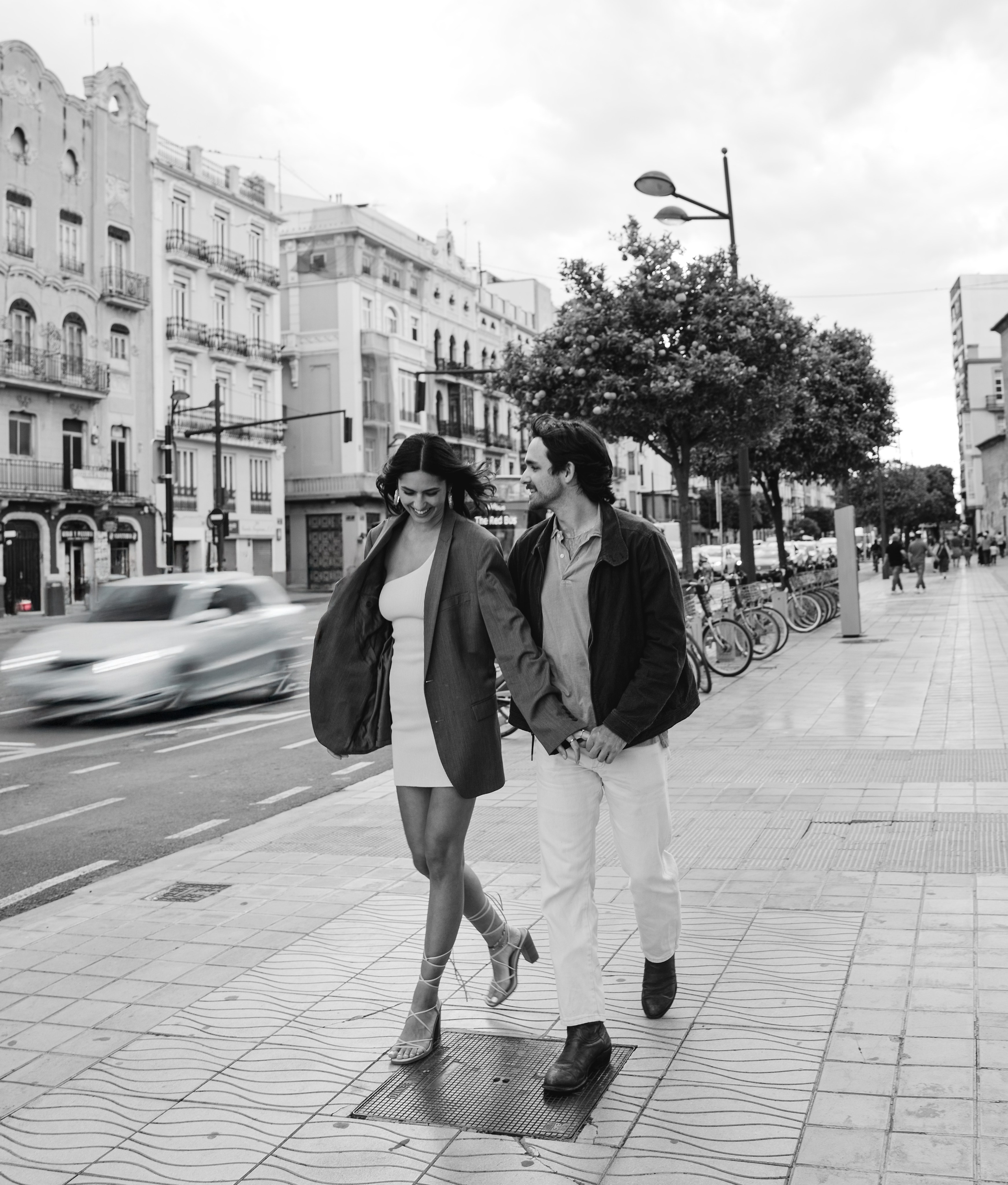 Romantic black-and-white street portrait of a couple walking hand in hand through the city center of Madrid, Spain — candid love story photography capturing urban charm, genuine connection, and joyful moments, perfect for couple photoshoots in Madrid and throughout Spain.