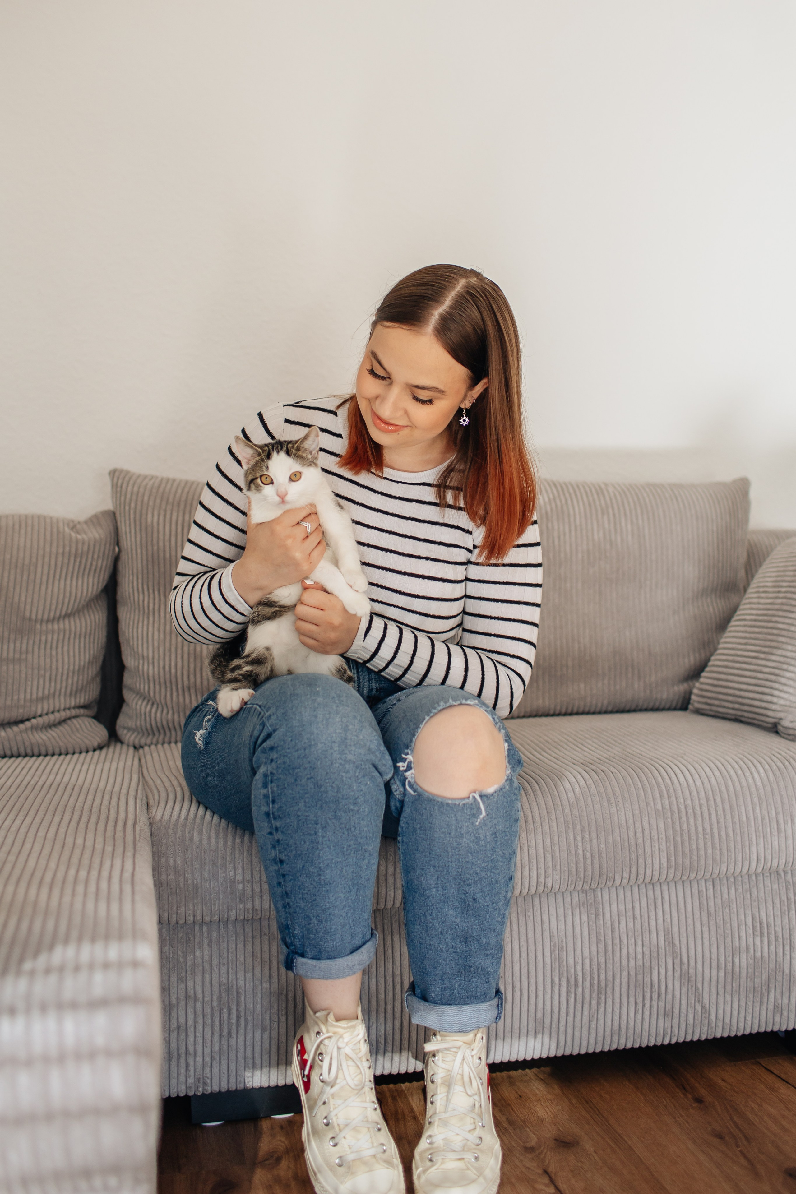 "Junge Frau sitzt auf dem Sofa und schaut ihr Kätzchen an"