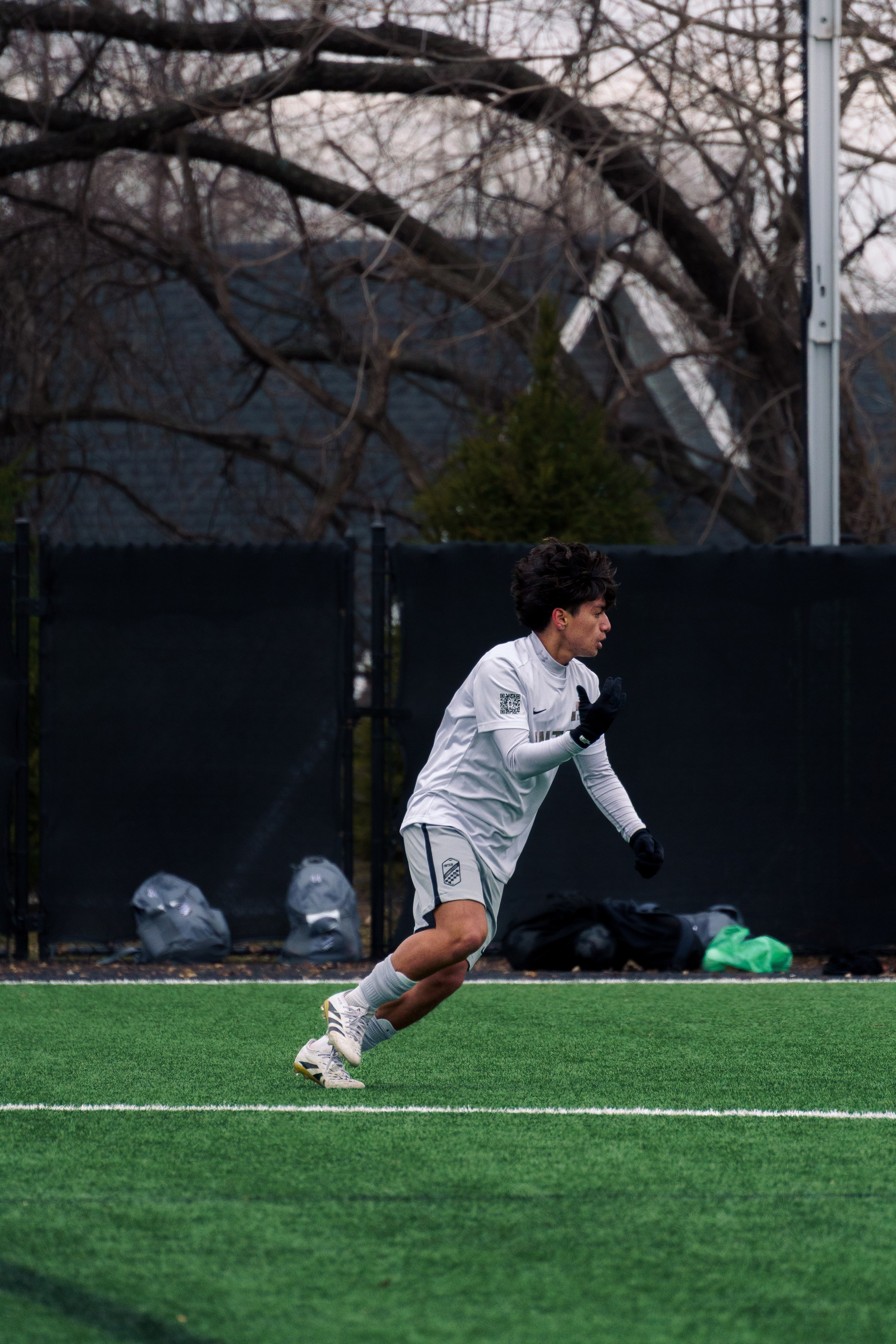Soccer player stopped mid-game raising his right hand in reaction to a play, appearing to signal or appeal to the referee.