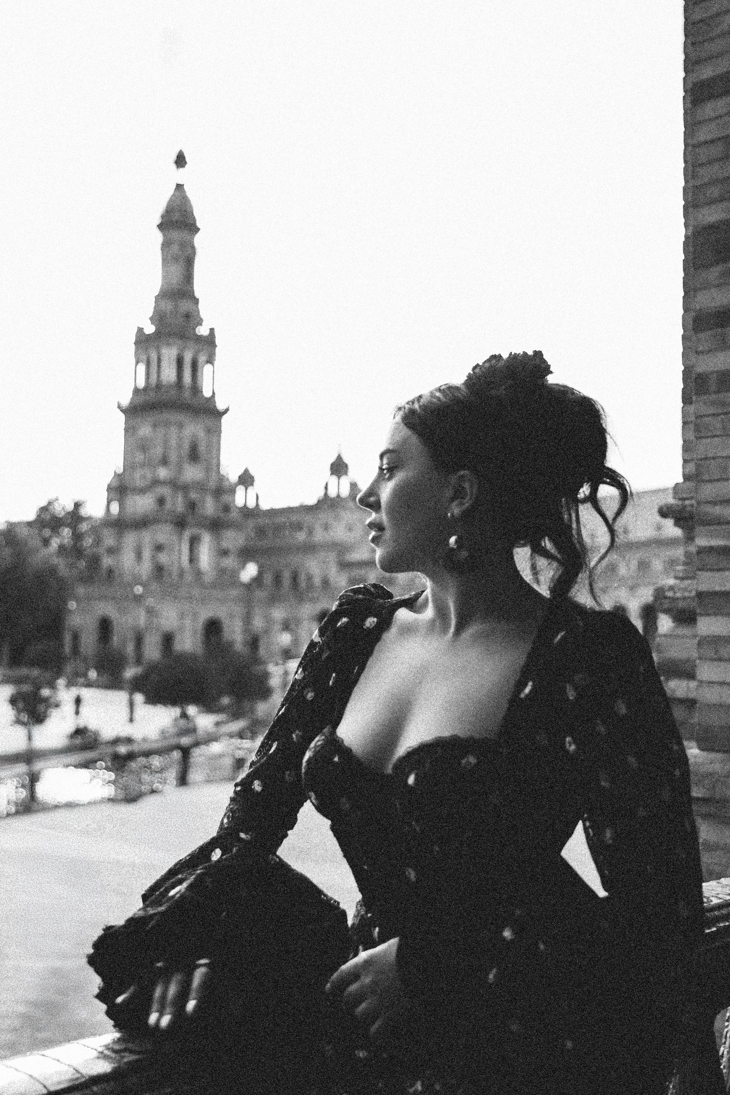 Элегантная женщина в винтажном черном платье позирует на фоне знаменитой Пласа-де-Эспанья в Севилье, Испания — вечная черно-белая портретная фотография, отражающая испанскую архитектуру, классическую красоту и романтичную атмосферу, идеально подходит для портретных фотосессий в Севилье и Испании.