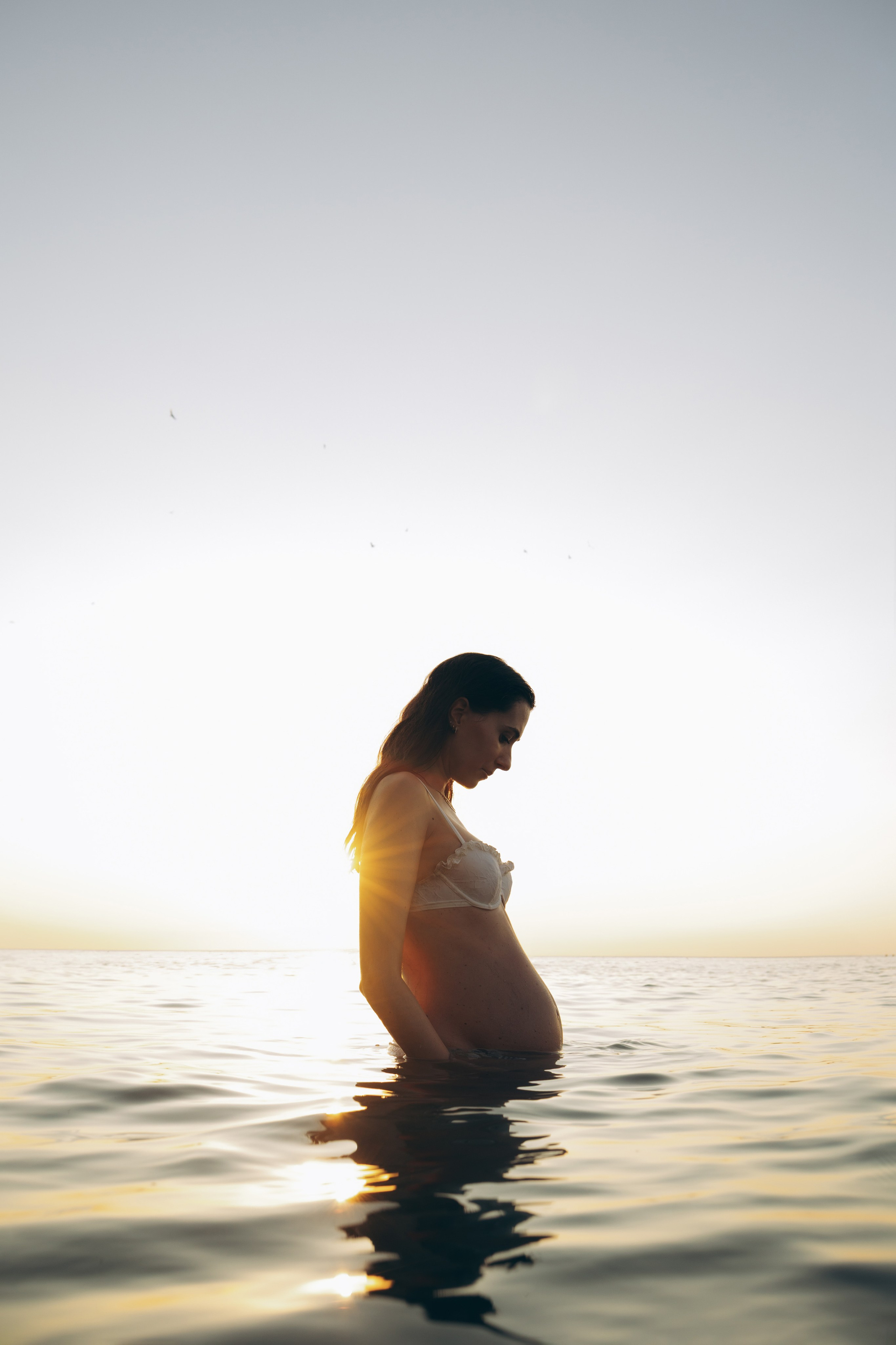 Donna incinta immersa nell’acqua al tramonto 