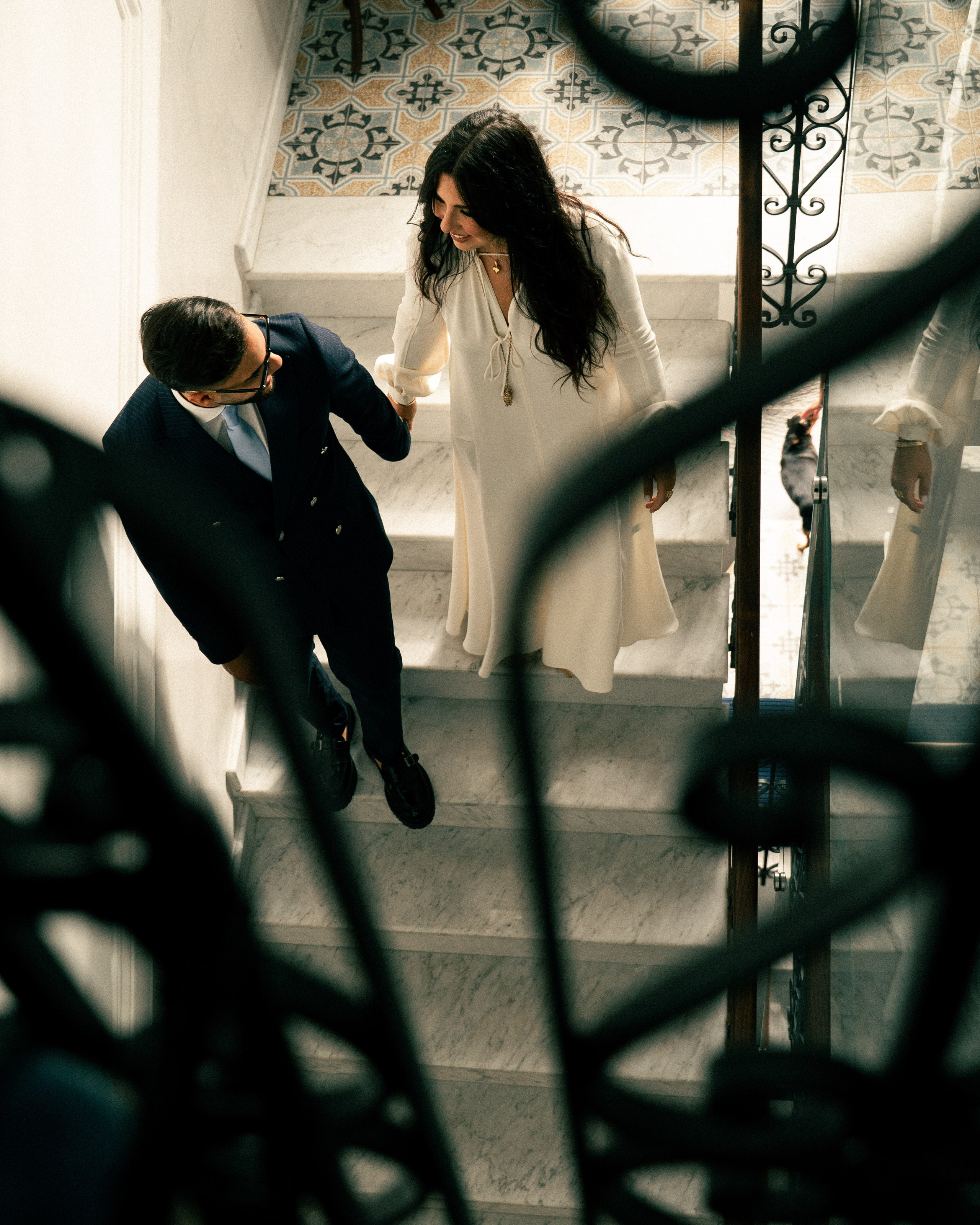 Bride and groom walking down the stairs, framed by the railing in the foreground