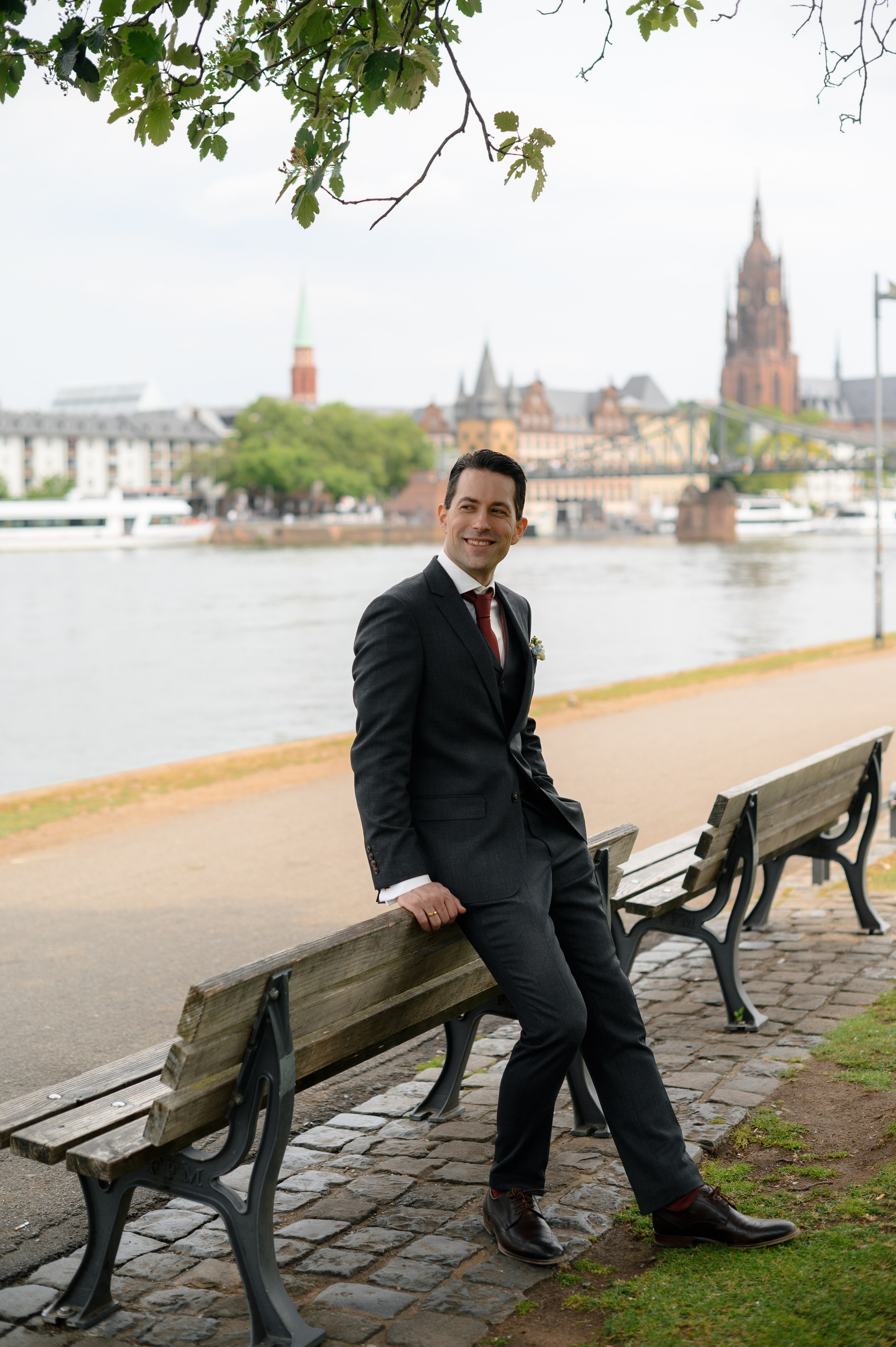 Bräutigam sitzt am Mainufer mit Blick auf Frankfurt und den Dom