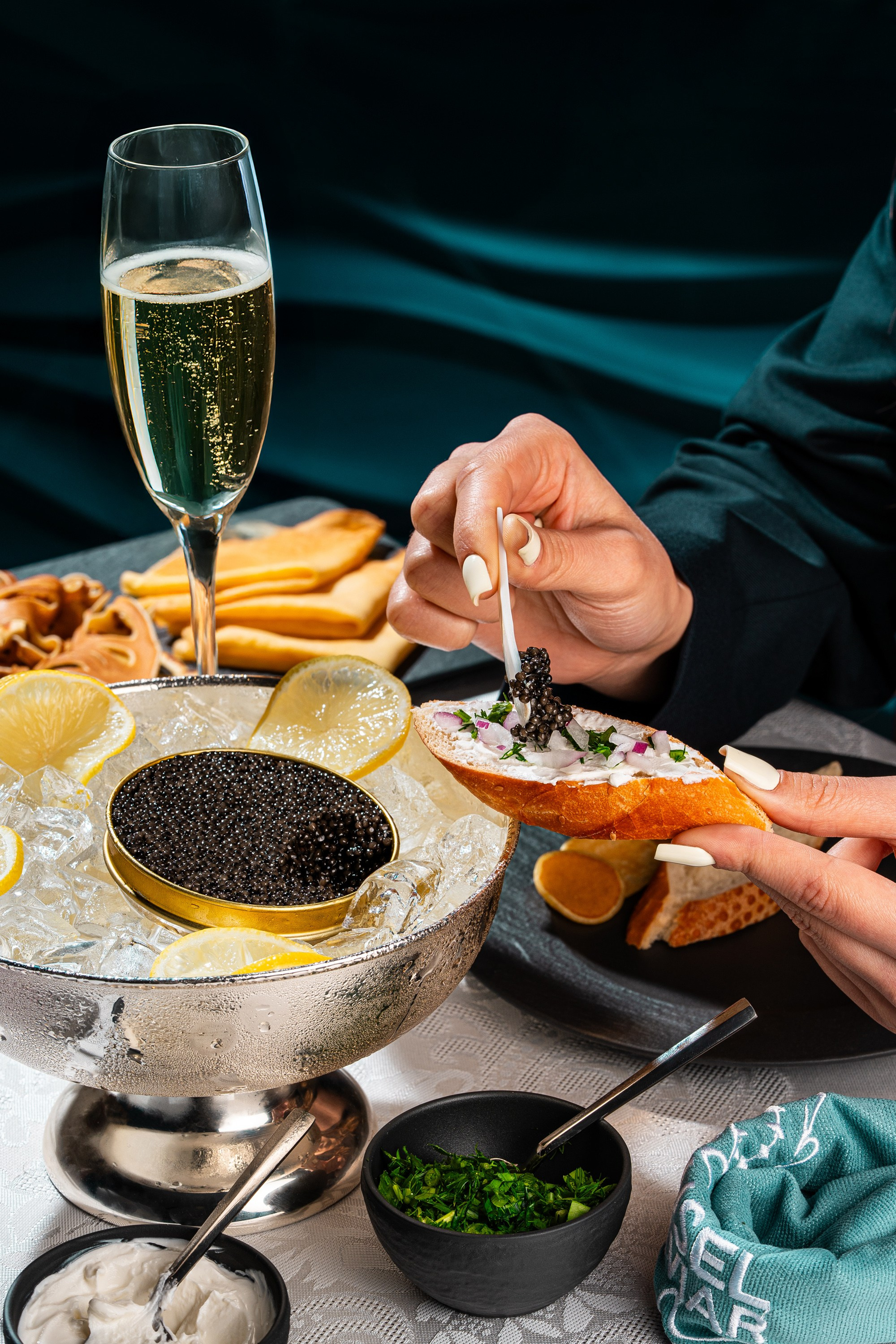 Kürü krem pendirli bagetin üzərinə, buz üzərində gümüş bir kasa kürü və bir stəkan şampan şərabının yanında yerləşdirən şəxs.