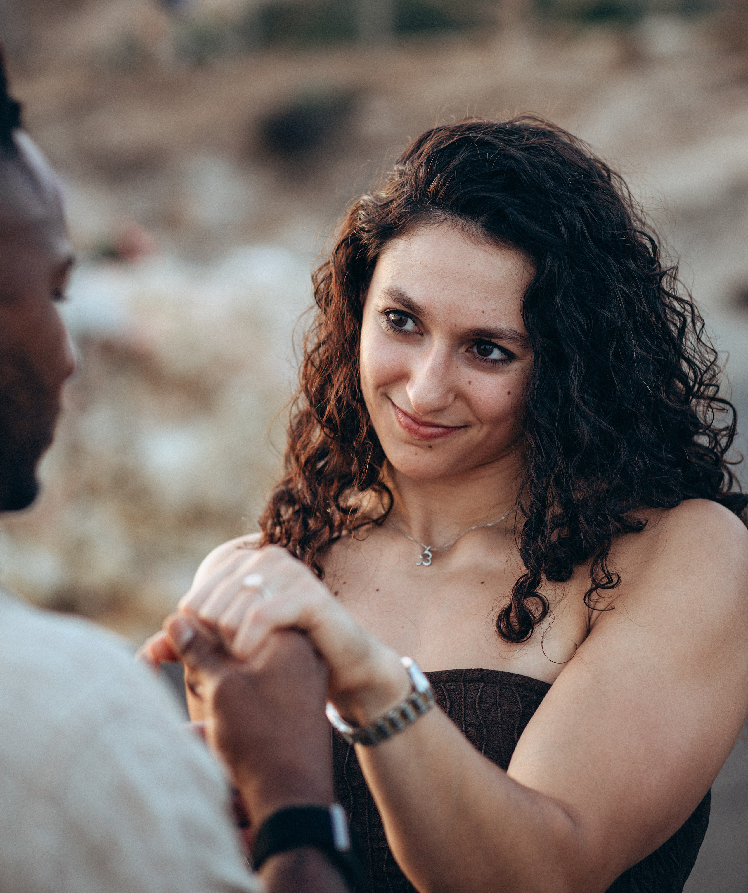 Momento emotivo durante una propuesta junto al mar en Valencia, España — una mujer mira con amor a su pareja mientras él coloca el anillo en su dedo. Ideal para quienes buscan sesiones íntimas y románticas de historia de amor en Valencia y en toda España.
