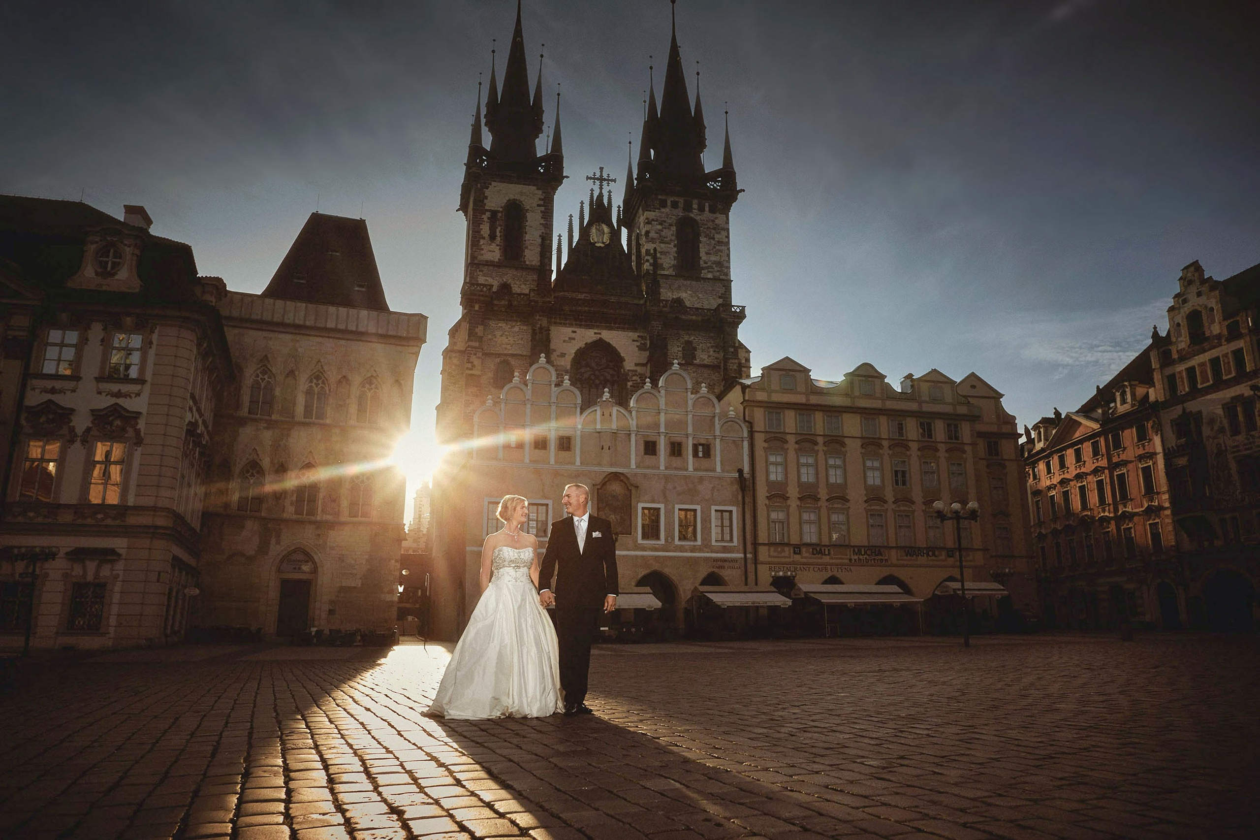 Sunlight beam highlighting a bride and groom walking through an alley in Prague's Old Town Square.