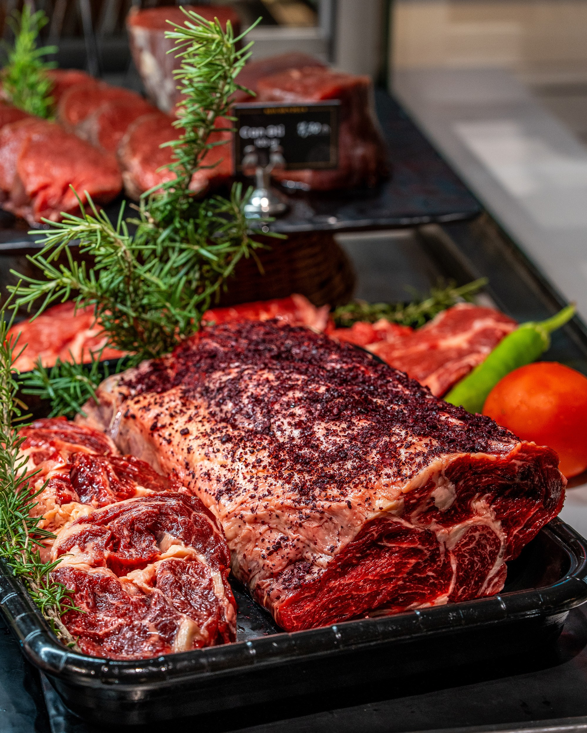 Qara istiot və ədviyyatla bol ovxalanmış, qalın, mərmərli mal əti parçası (ehtimal ki, antrikot/ribeye), tərəflərində ət tikələri, təzə rozmarin və pomidor/bibər.