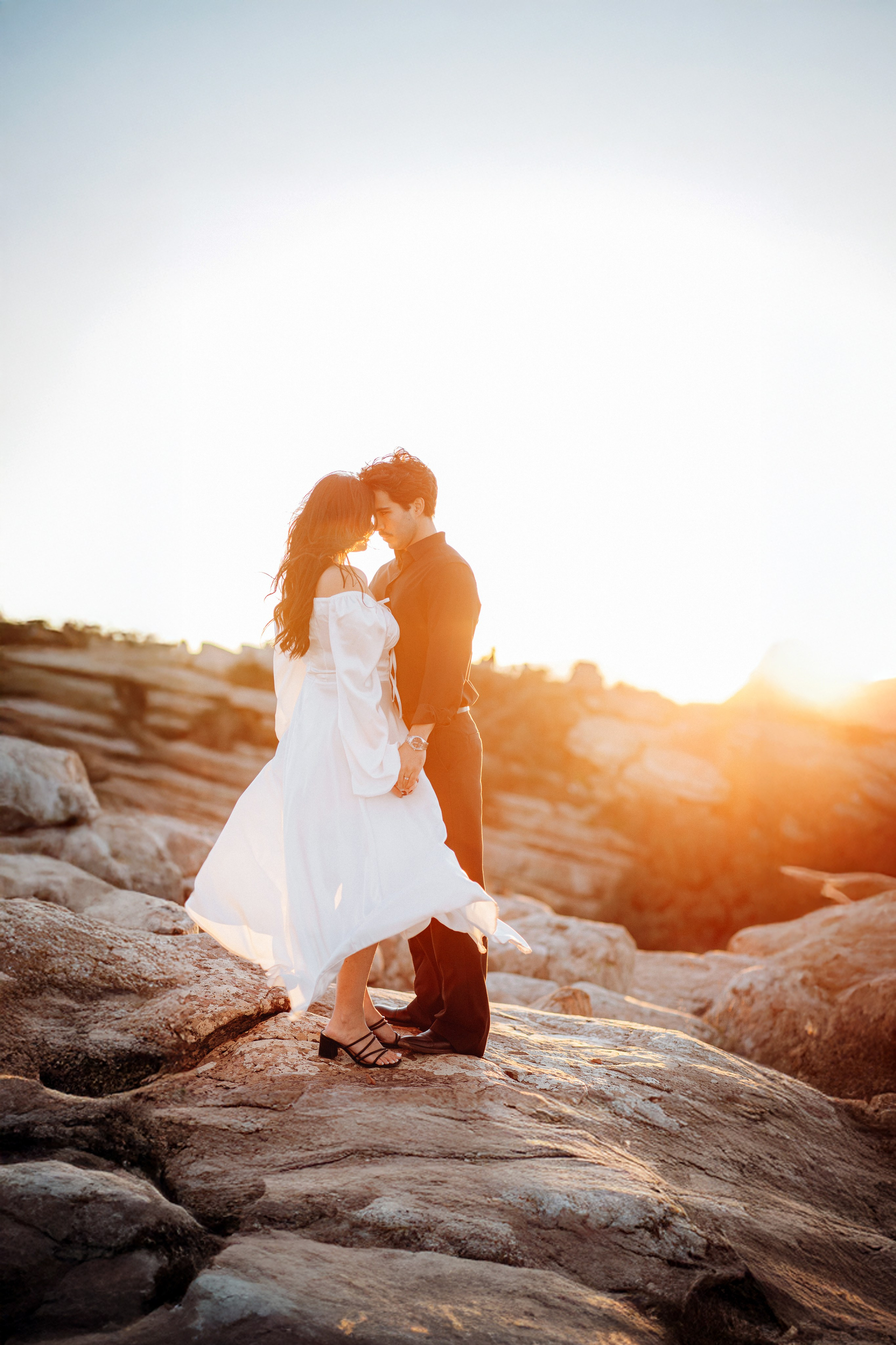 Bride and groom embracing on rocky cliffs at sunset during a private destination wedding in Barcelona, Spain. Warm golden light enhances the emotional connection of this intimate elopement moment.