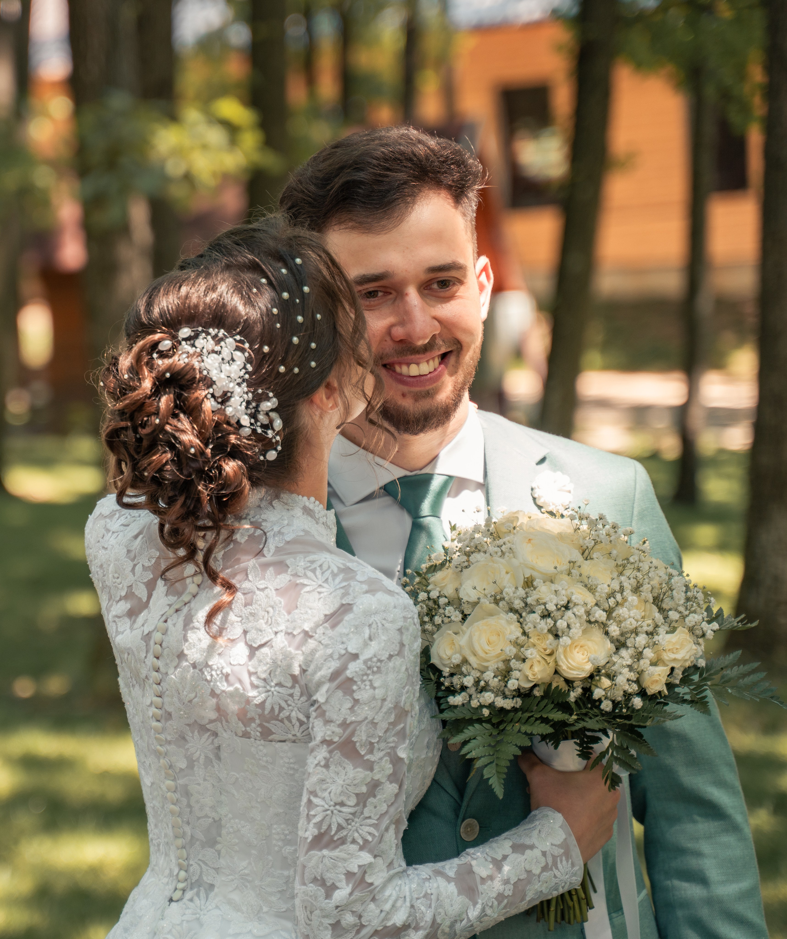 Mireasă cu rochie din dantelă și mire zâmbind, ținând un buchet de trandafiri albi, fotografie de nuntă incadru.ro.