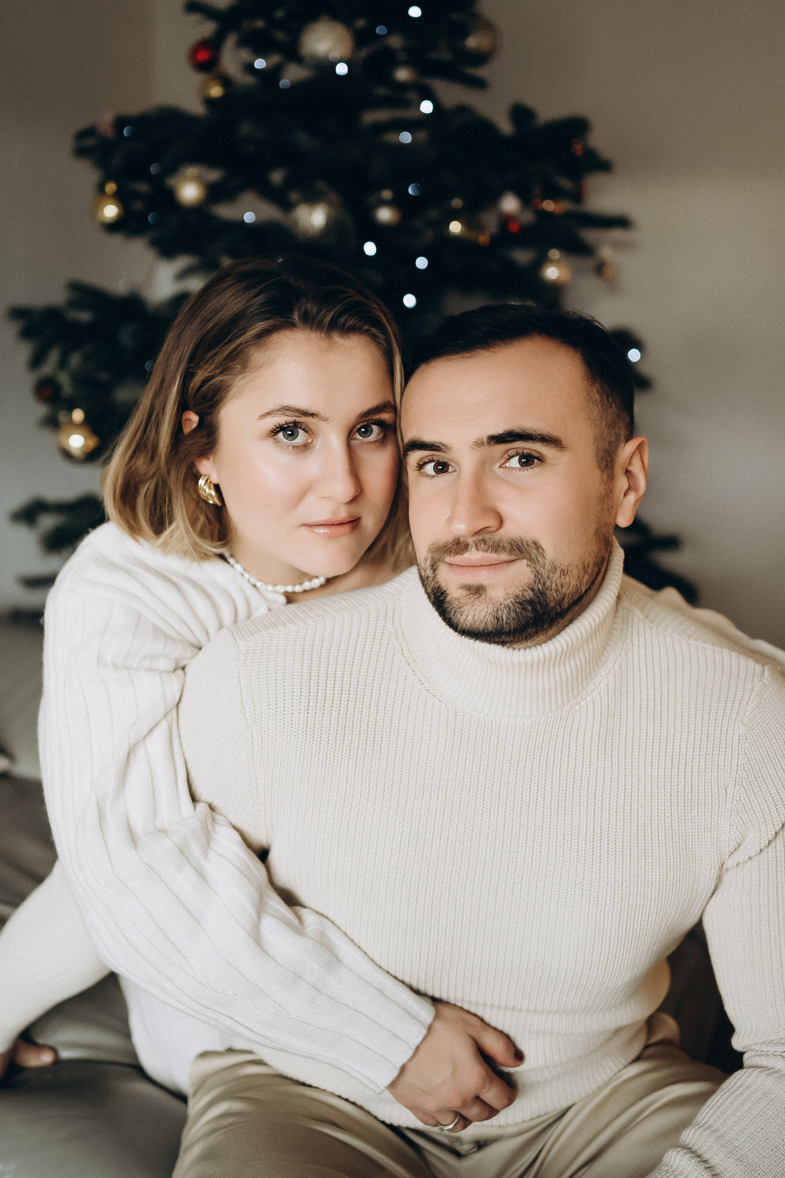 Die Frau umarmt liebevoll seinen Mann und beide schauen in die Kamera.