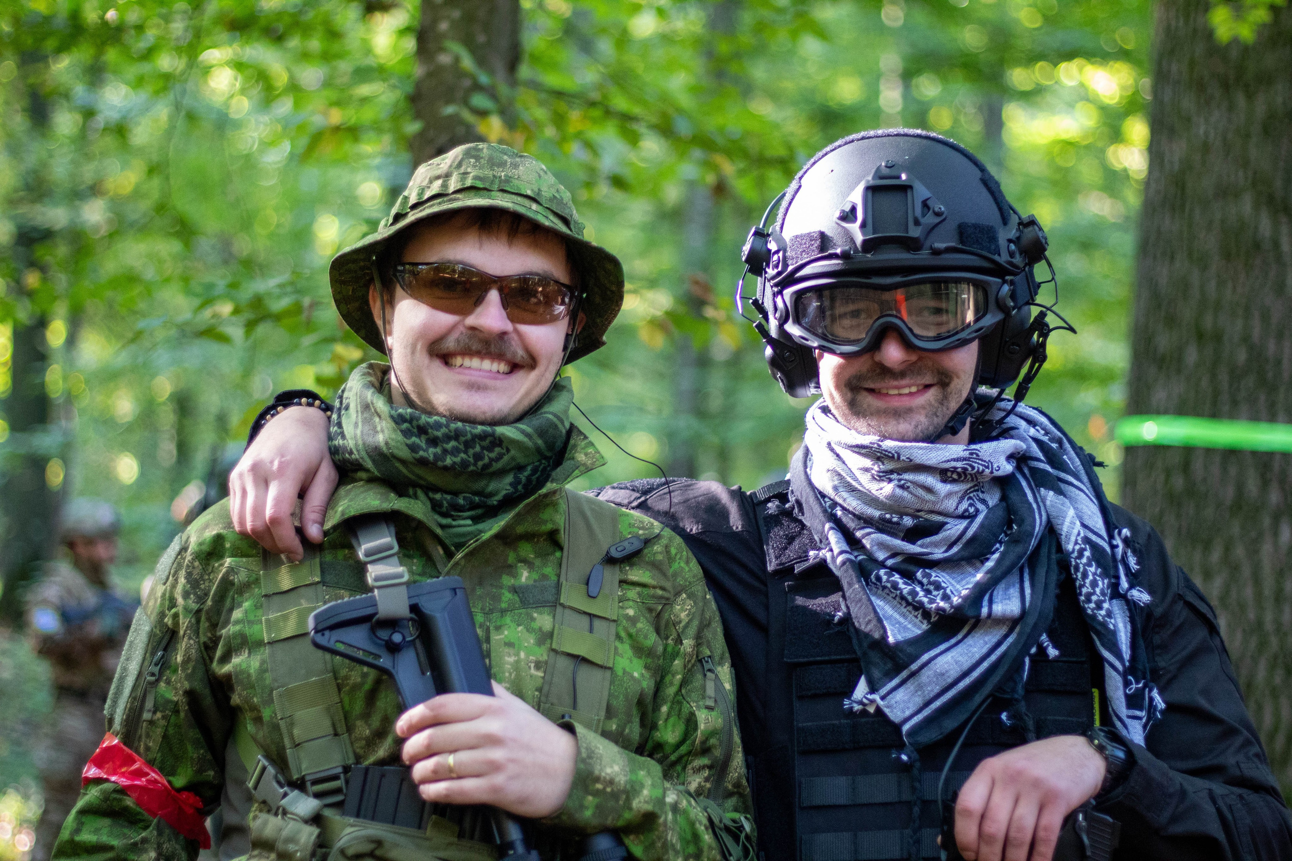Two people in camouflage and protective gear posing in character during an airsoft-themed shoot.