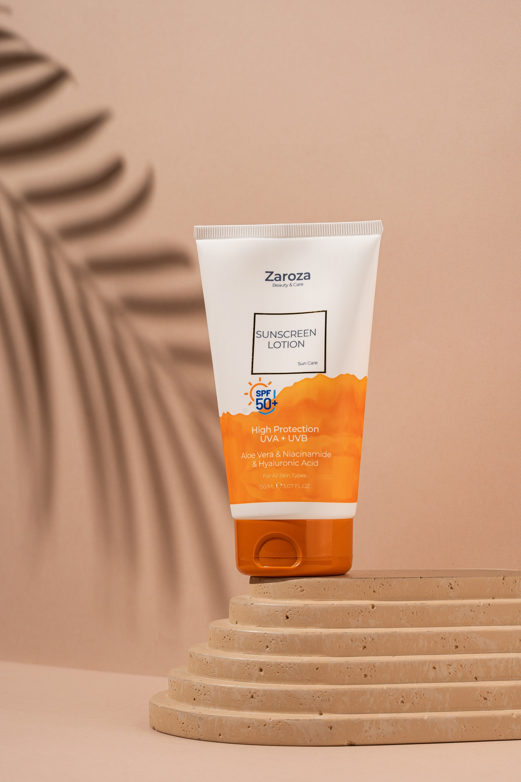 Zarozanın SPF 50+ Sunscreen Lotion kremi, bej fonda tropik yarpaq kölgəsi ilə mərmərvari pillə üzərində təqdimat.