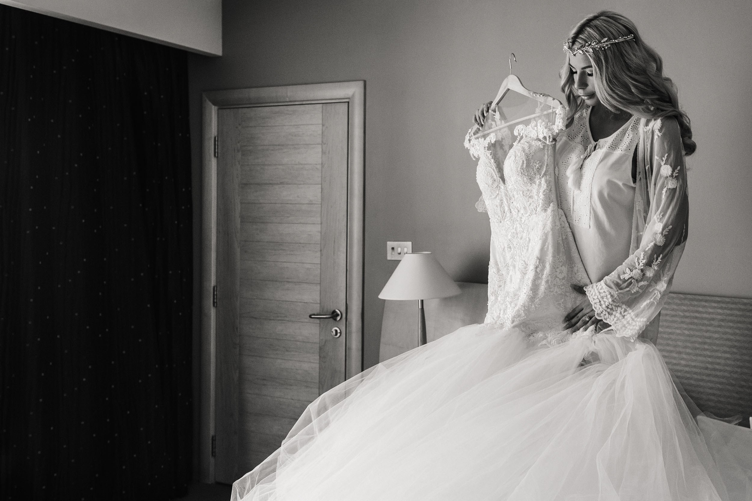 Bride is holding her wedding dress in a hotel room 