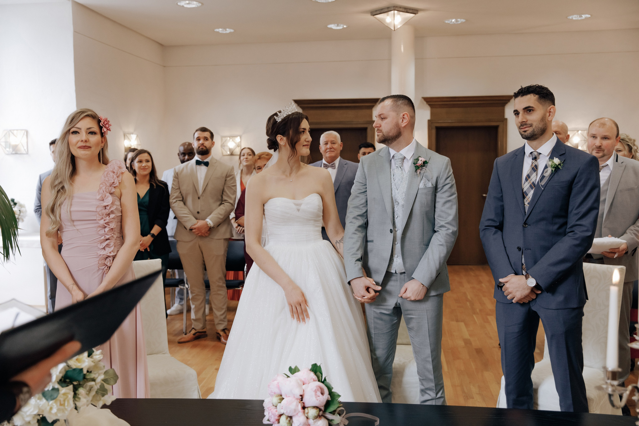 Der Bräutigam und die Braut schauen sich verliebt an, während die Gäste der Rede der Standesbeamtin zuhören.