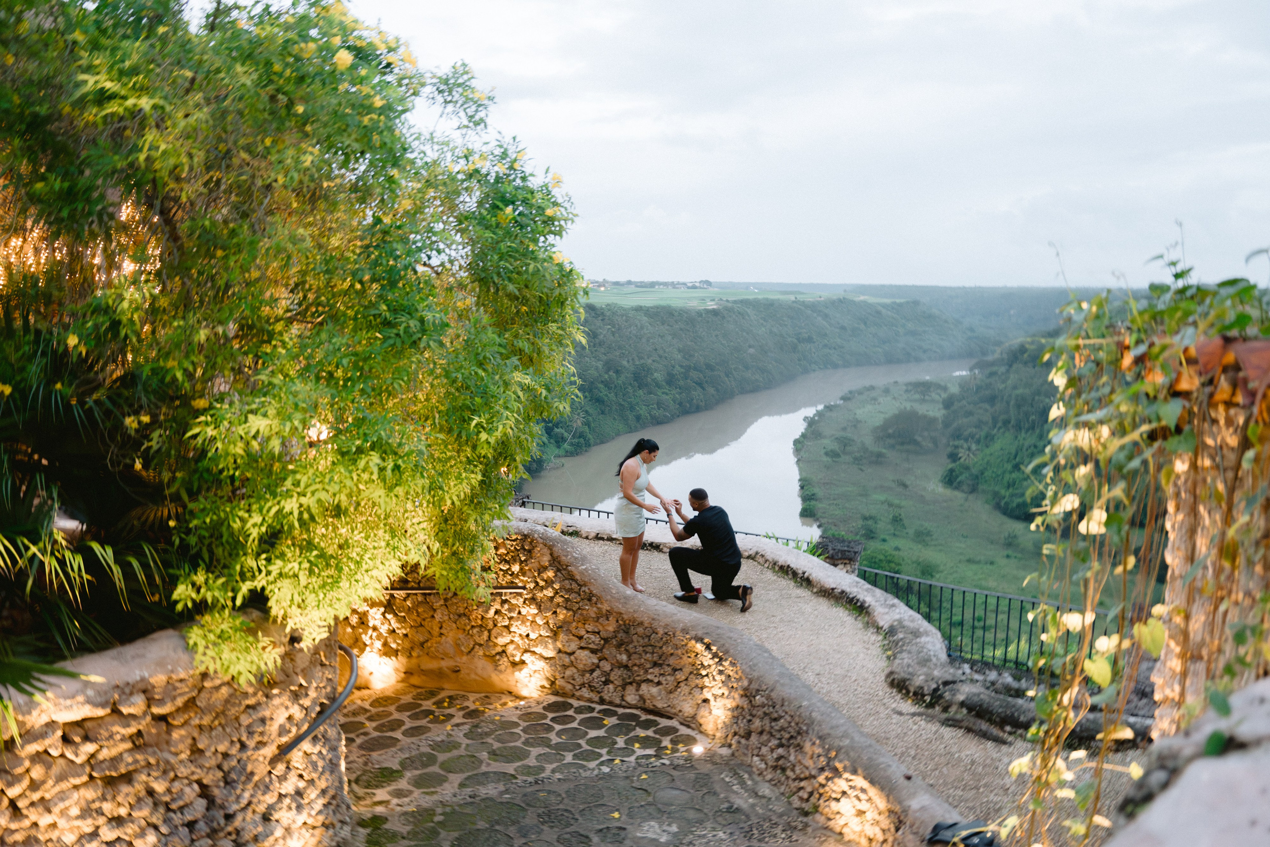 Man proposing to a woman at a scenic overlook with a river valley in the background, surrounded by rustic stone of Altos de chavon. Punta cana wedding family fashion photographer dominican republic, destination wedding photographer, elopement photography Punta Cana