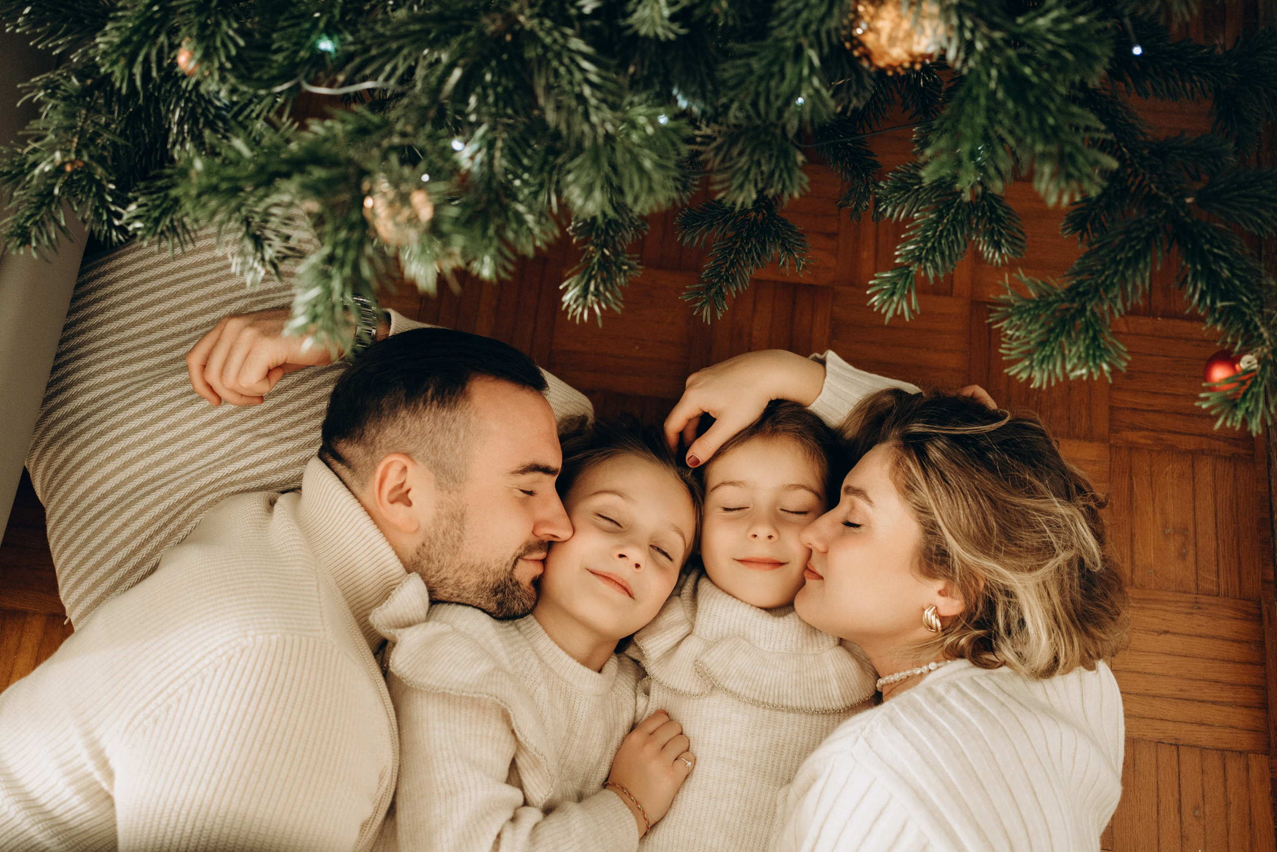 Eine Familie kuschelt sich auf dem Boden unter einem Weihnachtsbaum.