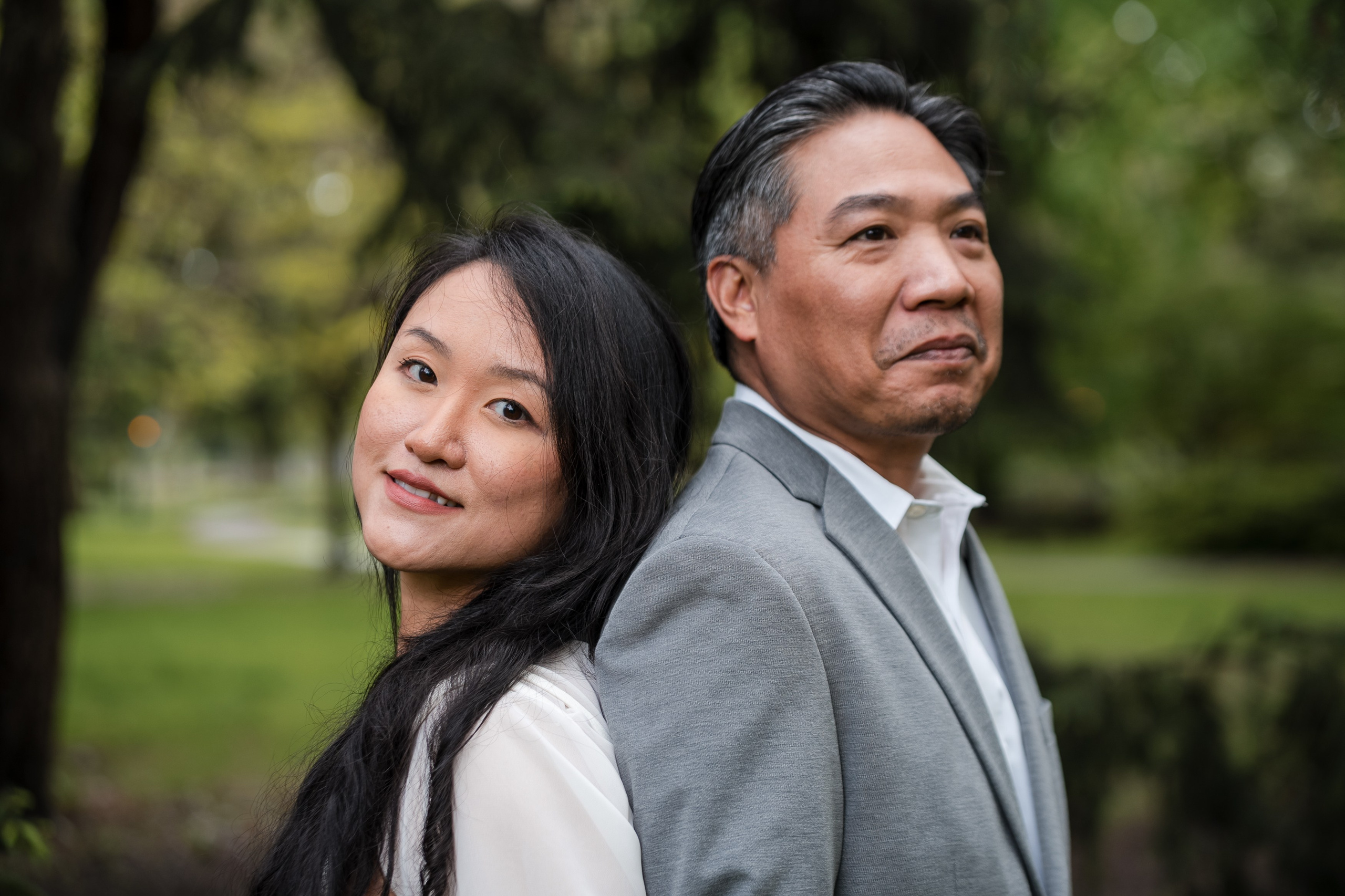 Engaged couple standing back to back in a forest, smiling softly during their engagement photoshoot.