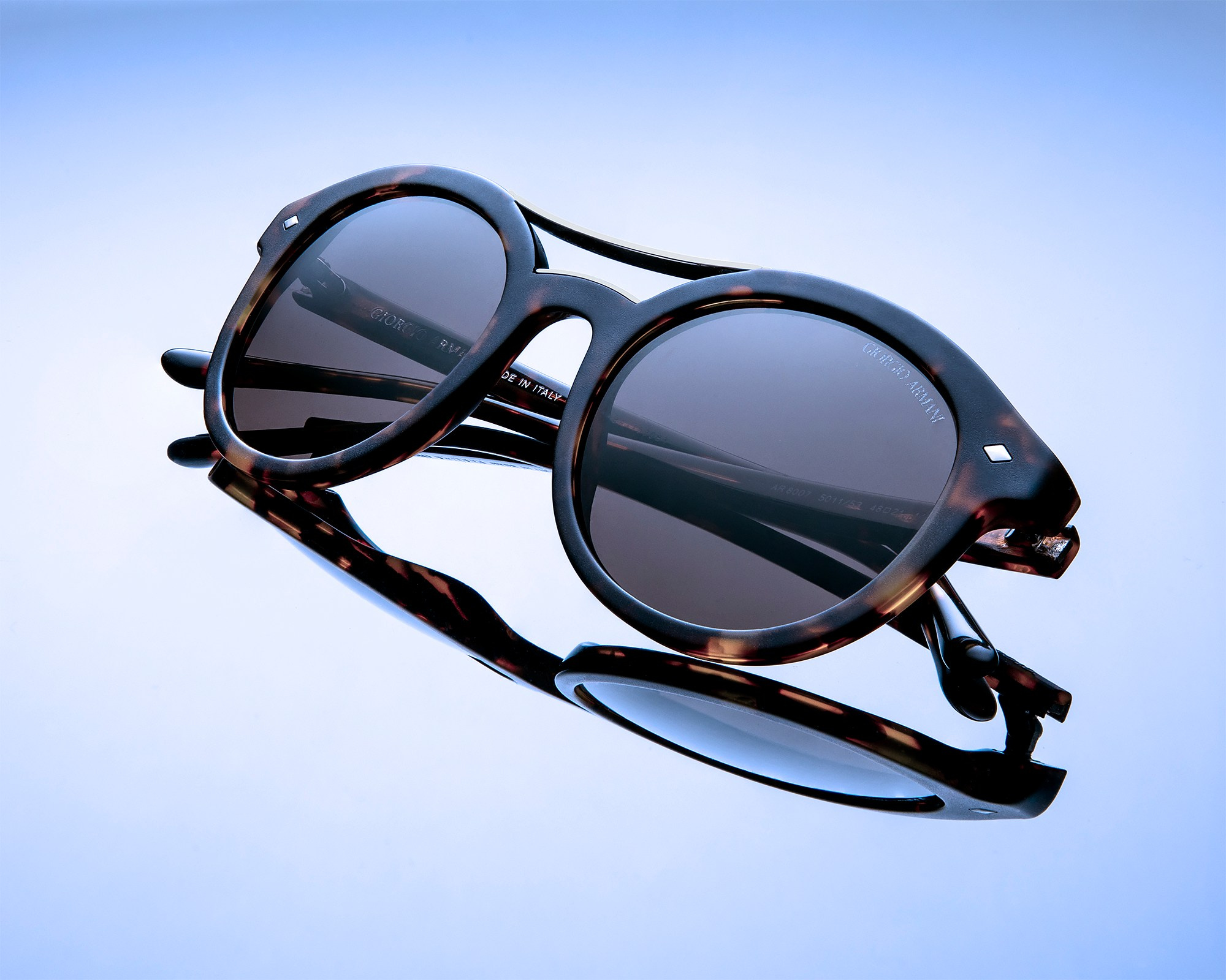 Photographer Roman Djuzev - Sunglasses from the brand Emporio Armani close-up on a blue background with reflection.