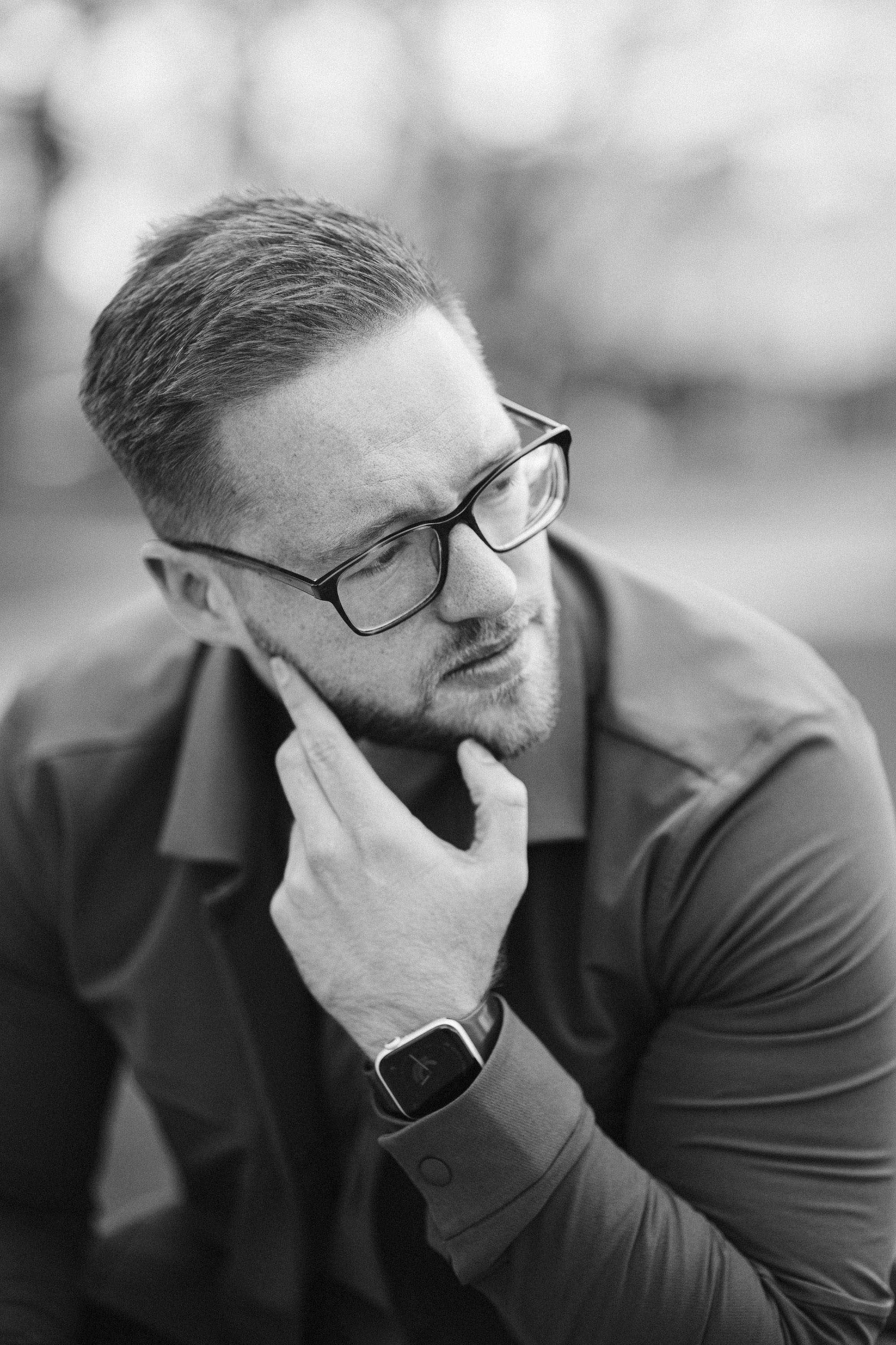 Black-and-white portrait of man in glasses thinking, hand on chin