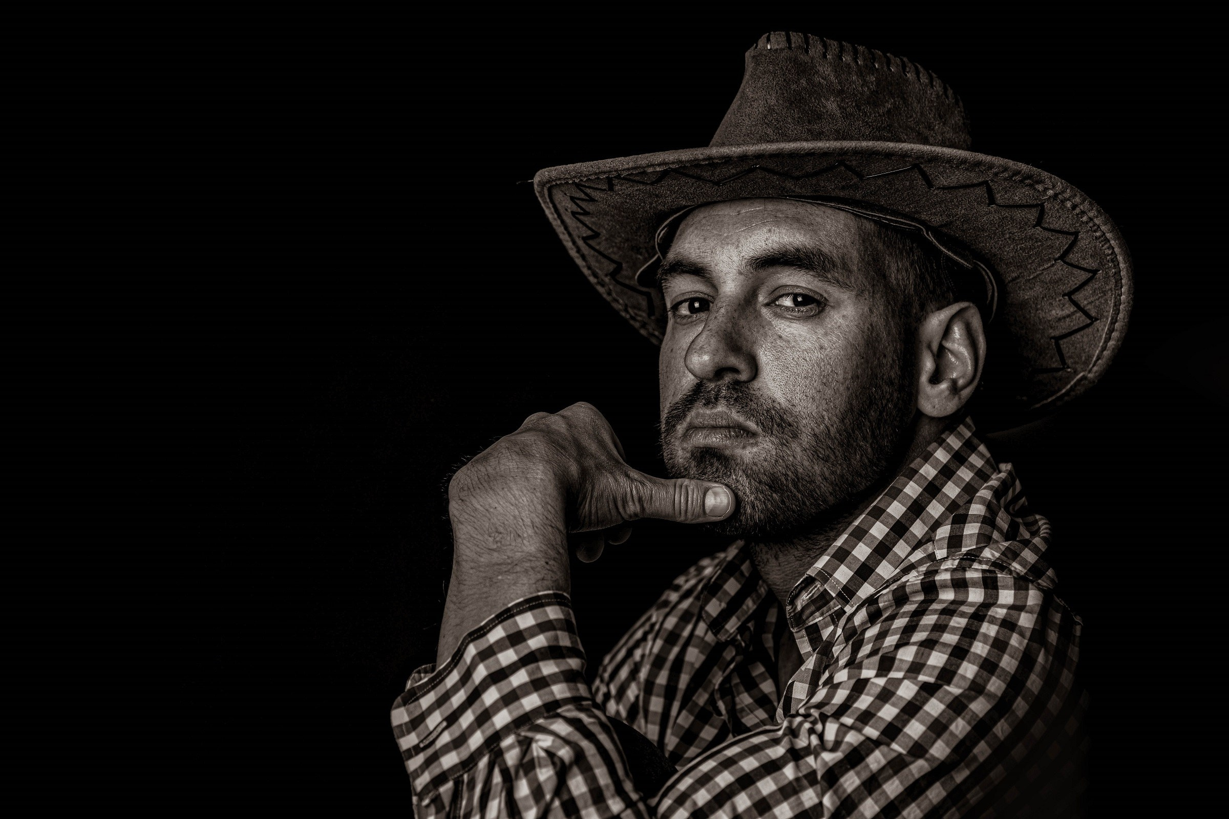 Black and white portrait of a man wearing a hat, resting his chin on his hand