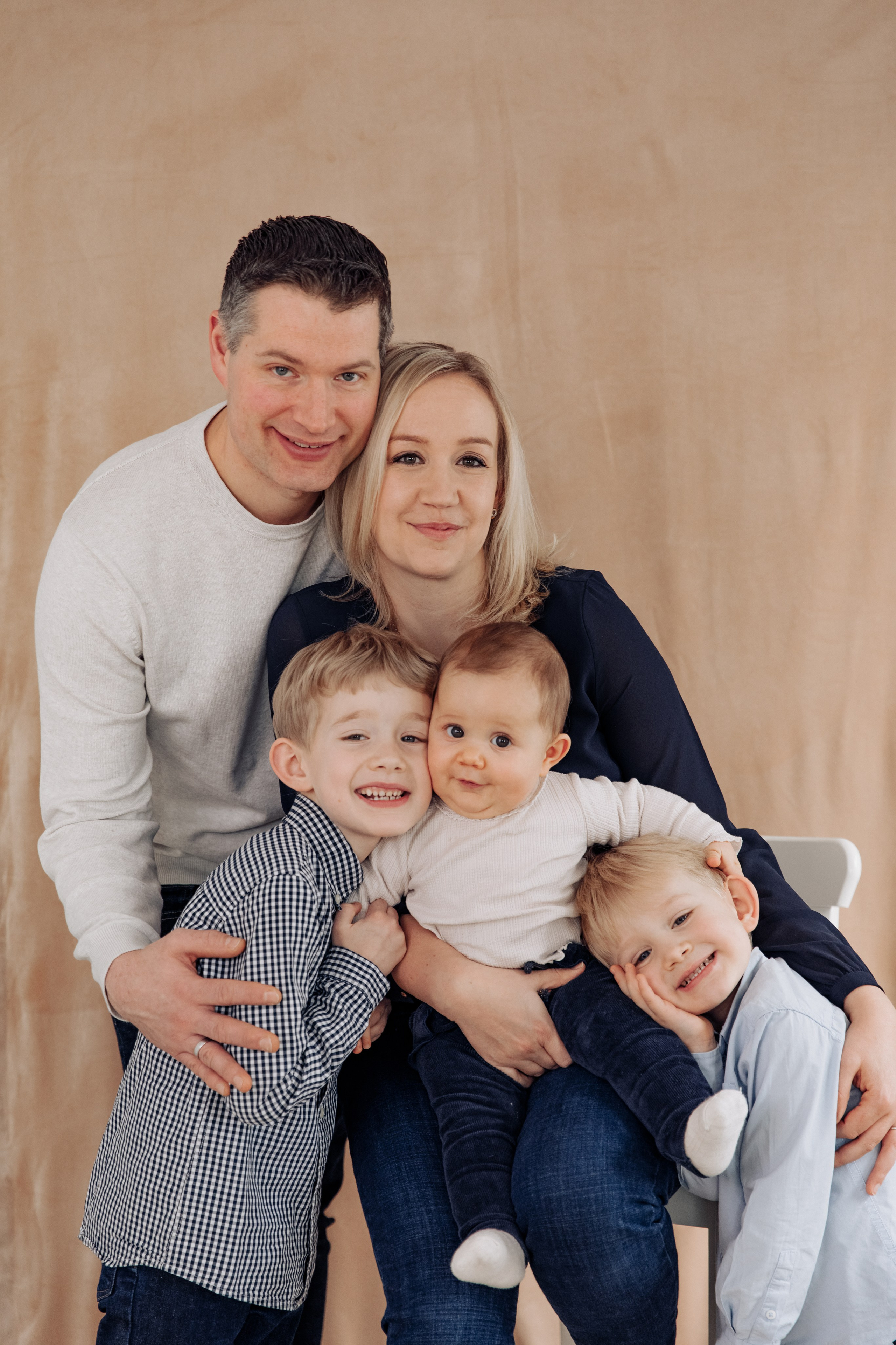Glückliche Familie beim Fotoshooting im Studio: Eltern mit zwei Söhnen und einem kleinen Mädchen vereint auf einem Familienporträt.
