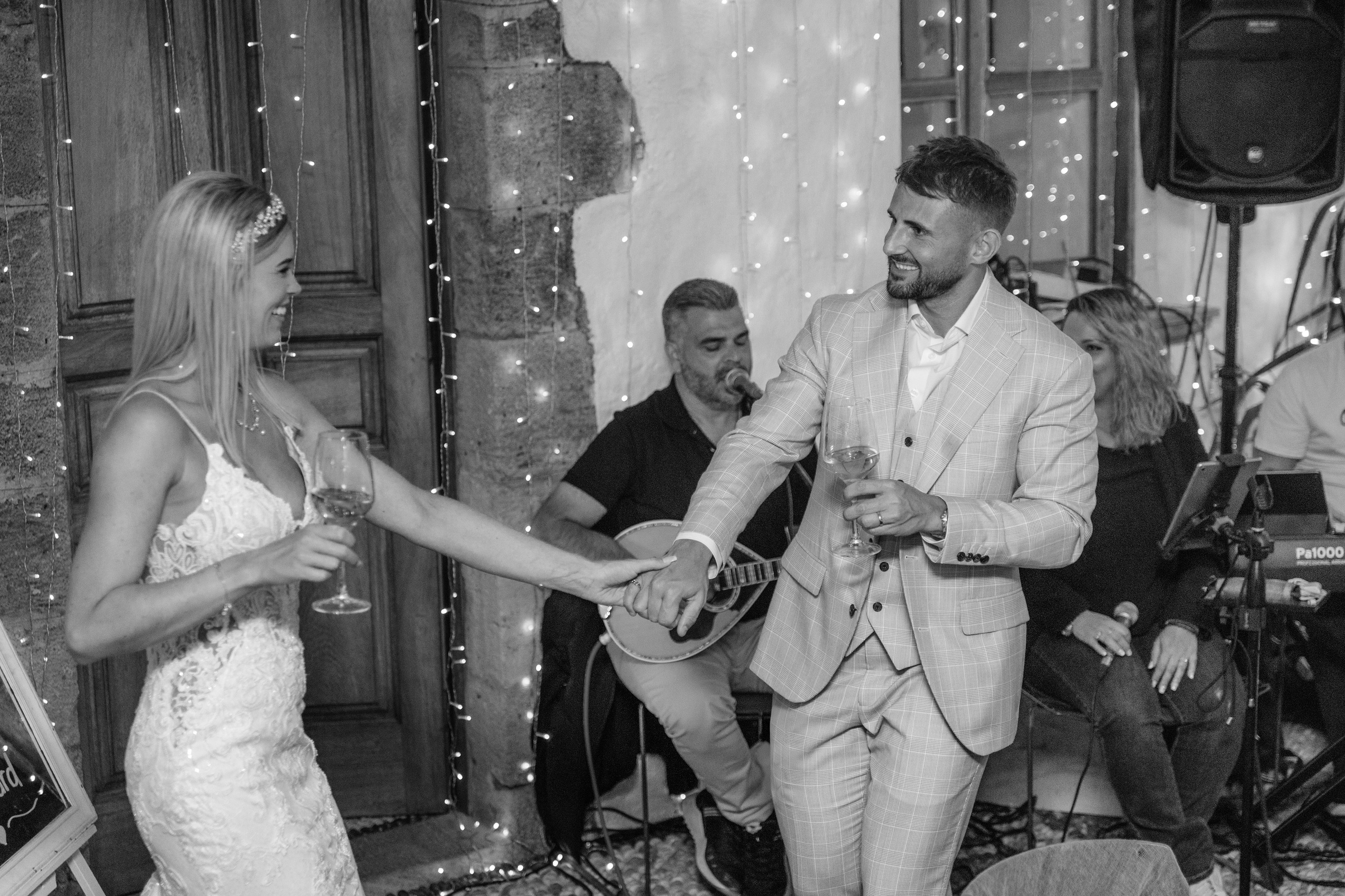 Bride and groom dancing together during their wedding party at a beautifully decorated restaurant in Lindos, Greece, with guests cheering around them.