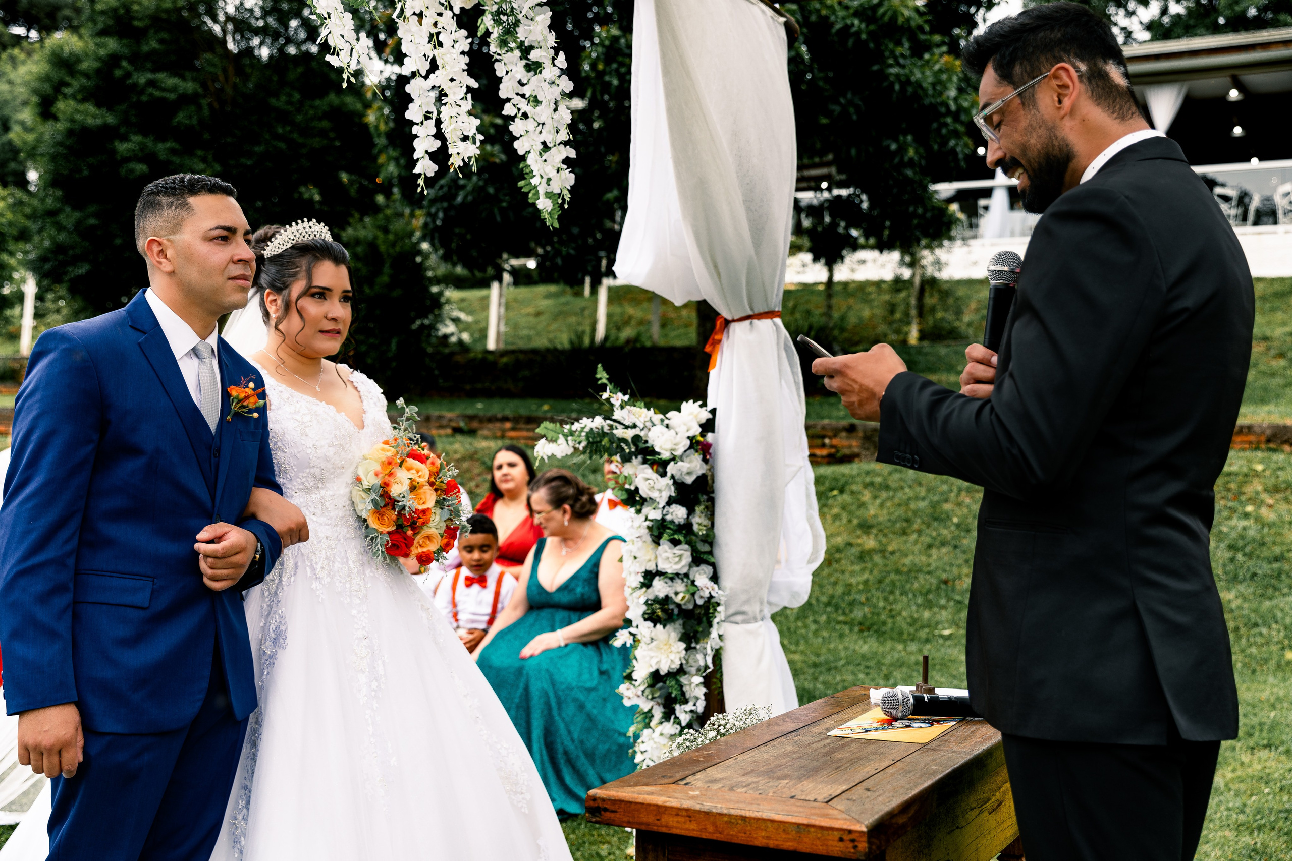Noivos de mãos dadas durante a cerimônia de casamento, concentrados na fala do celebrante.