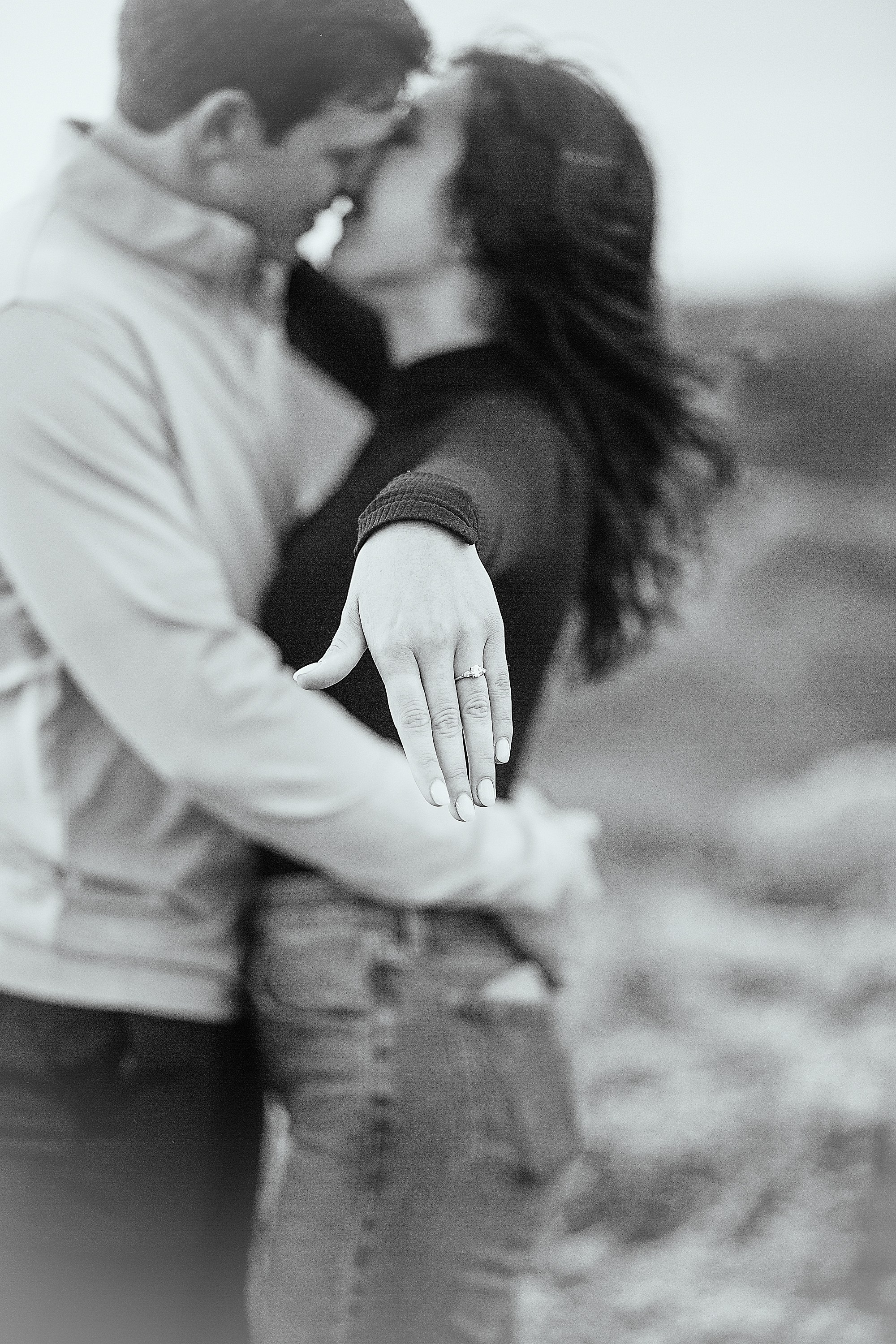 A romantic black and white portrait of a couple holding each other closely in a coastal landscape in Ireland.