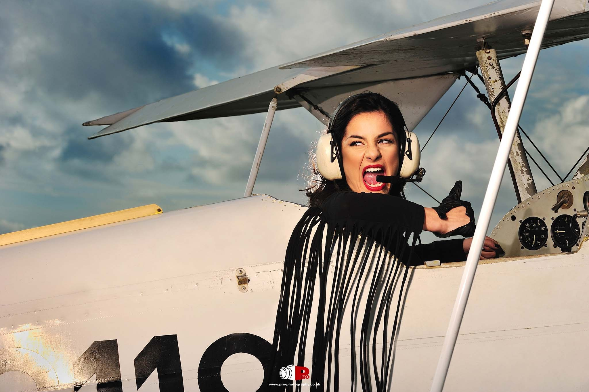 A bold woman wearing pilot gear posing inside a vintage aircraft.