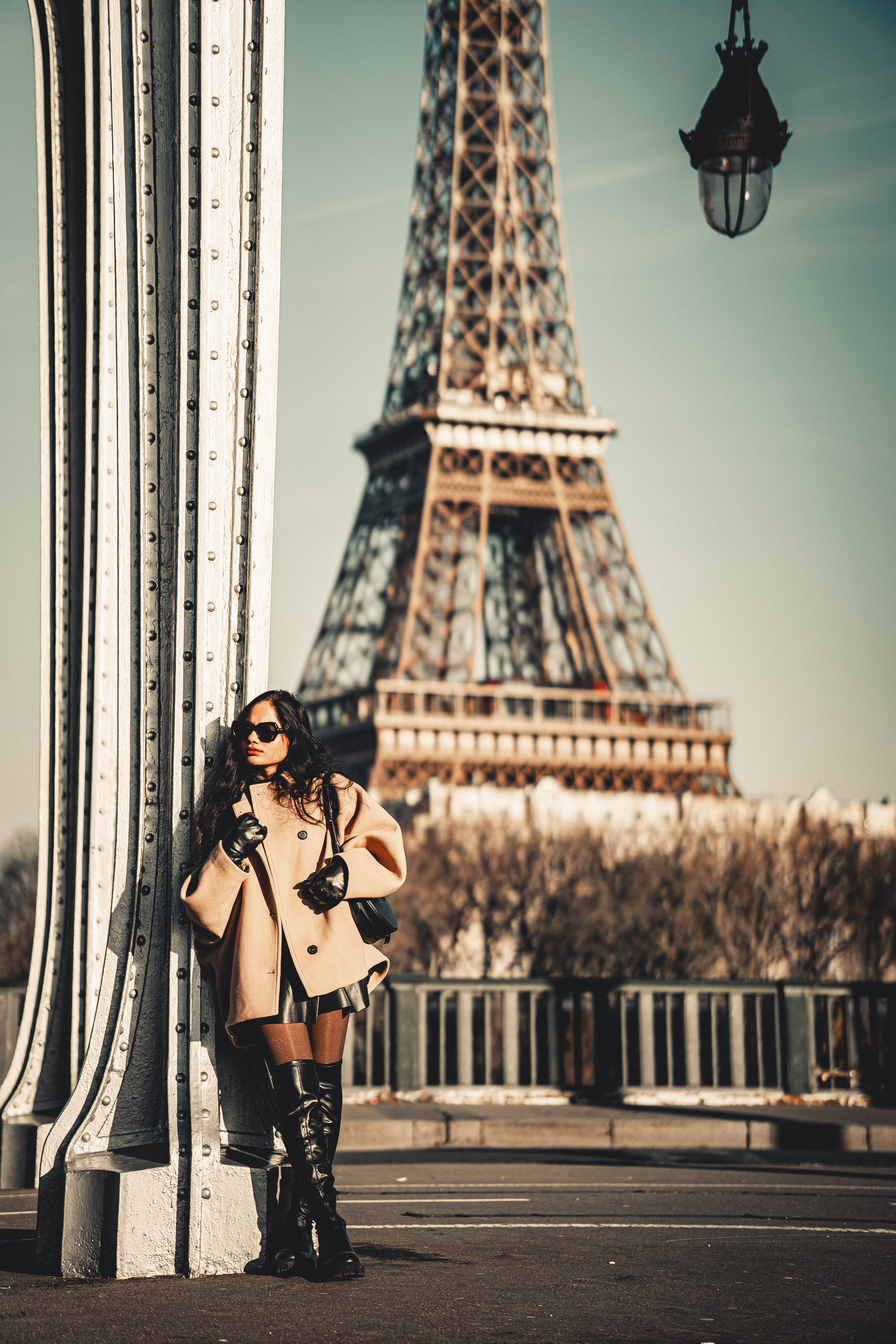 a woman wearing oversized brown jacket and standing with paris bridge and eiffel tower view behind her