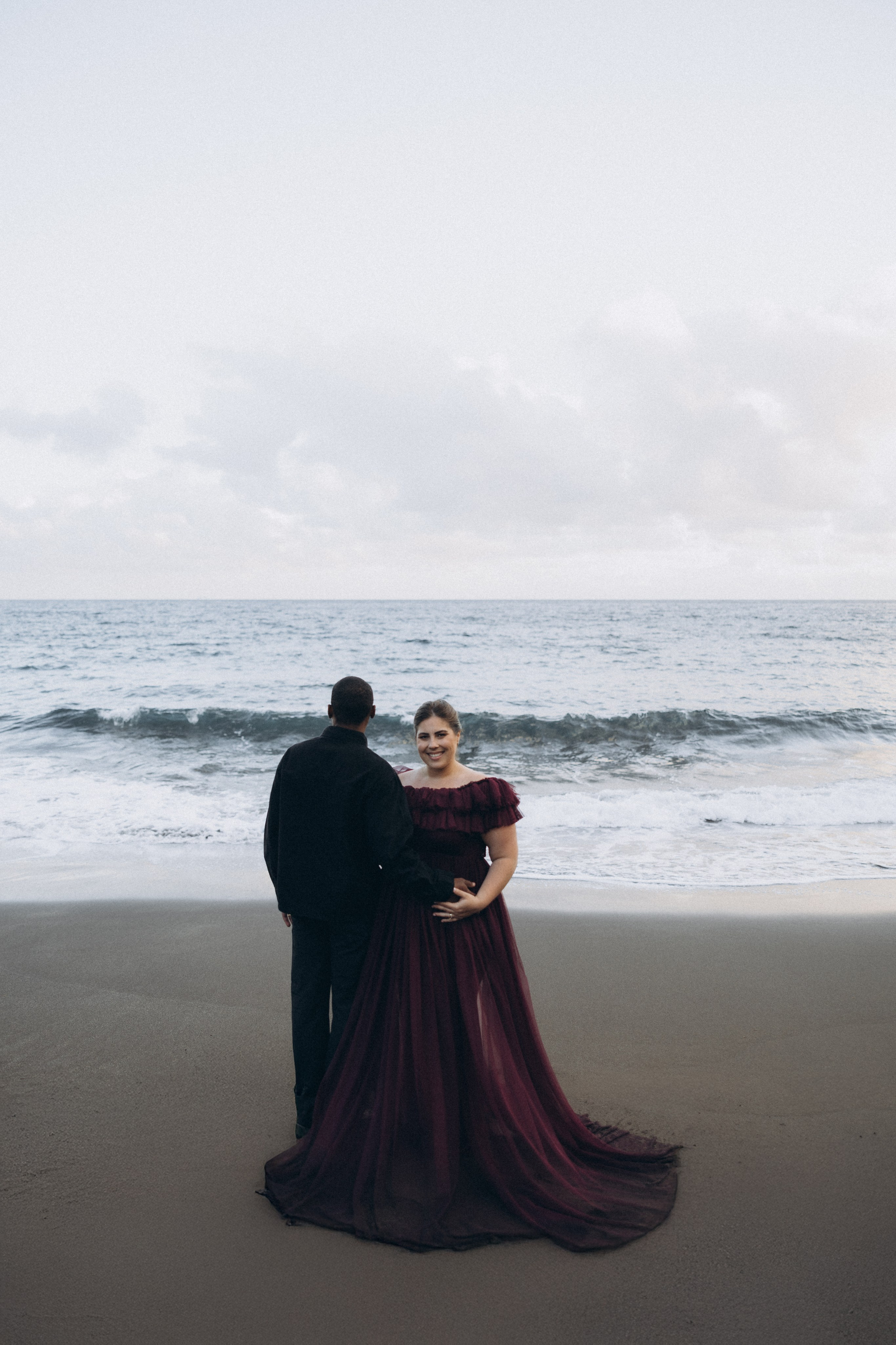 A glowing expectant mother standing on a cliff overlooking the ocean in Madeira, her dress flowing gently in the wind as the golden sunset casts a warm glow.
