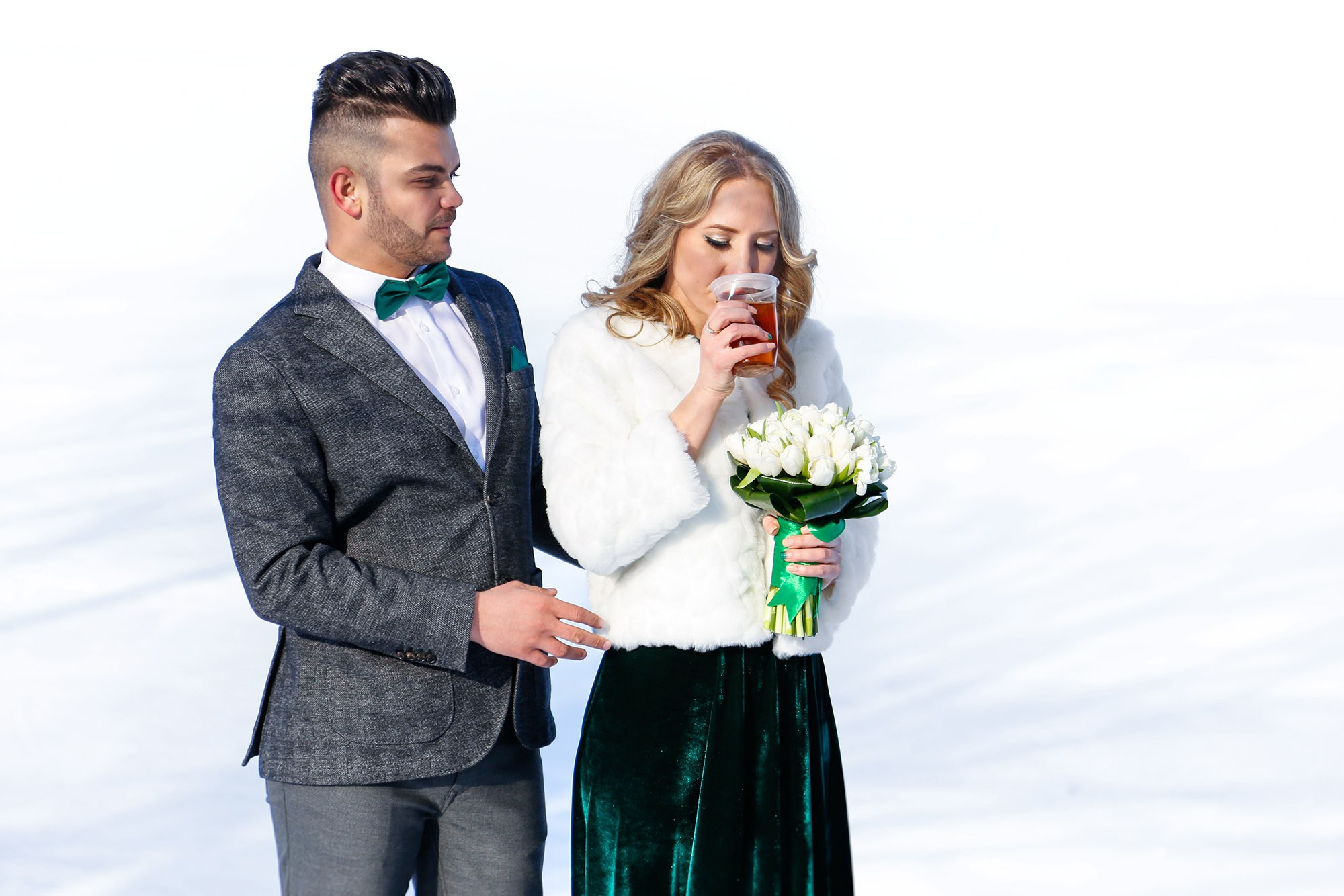 Creative shot of the smiling bride enjoying a hot tea from a white mug to keep warm during her winter photo shoot.
