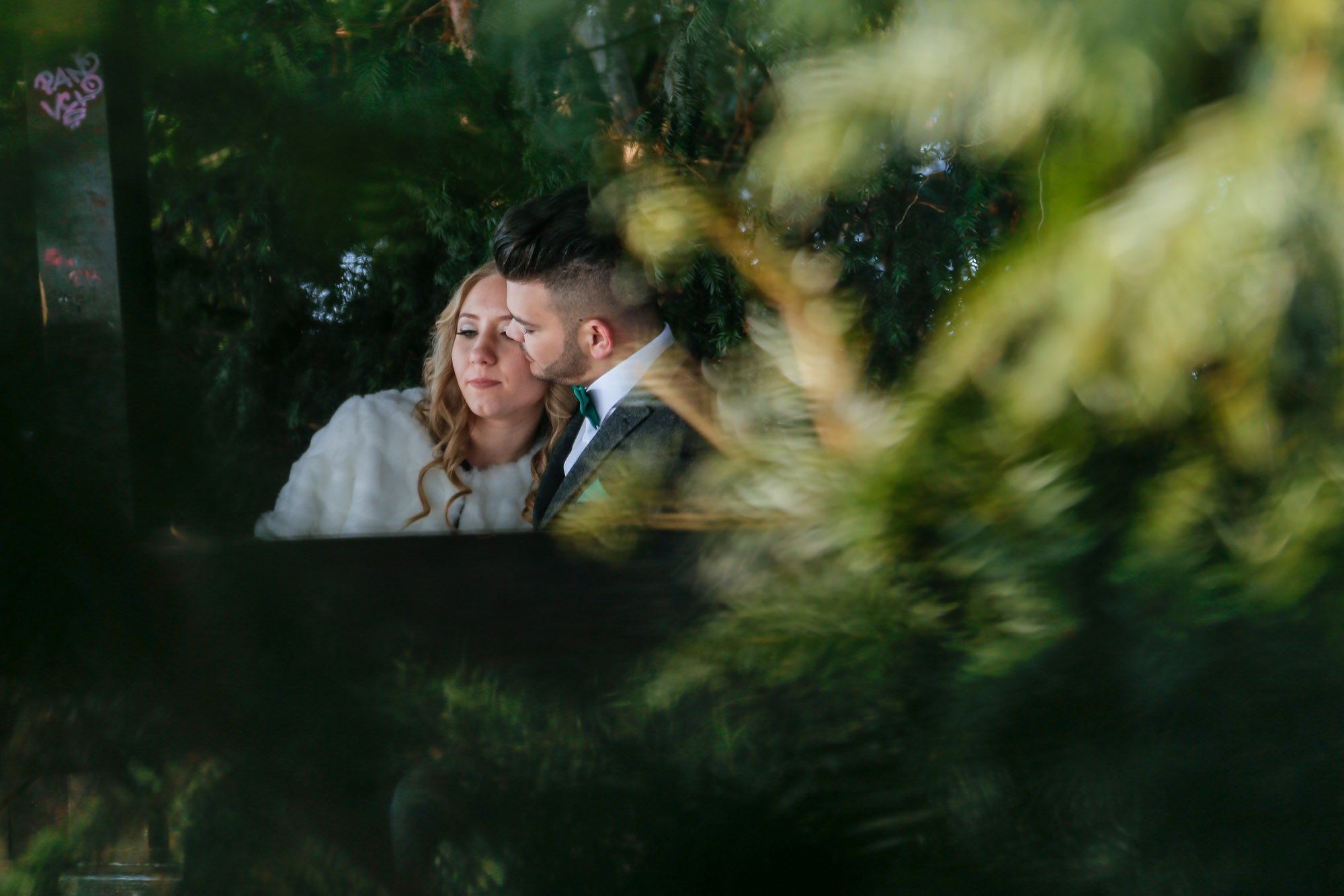 Creative wedding composition featuring the couple subtly framed through green leaves, creating a striking visual contrast.
