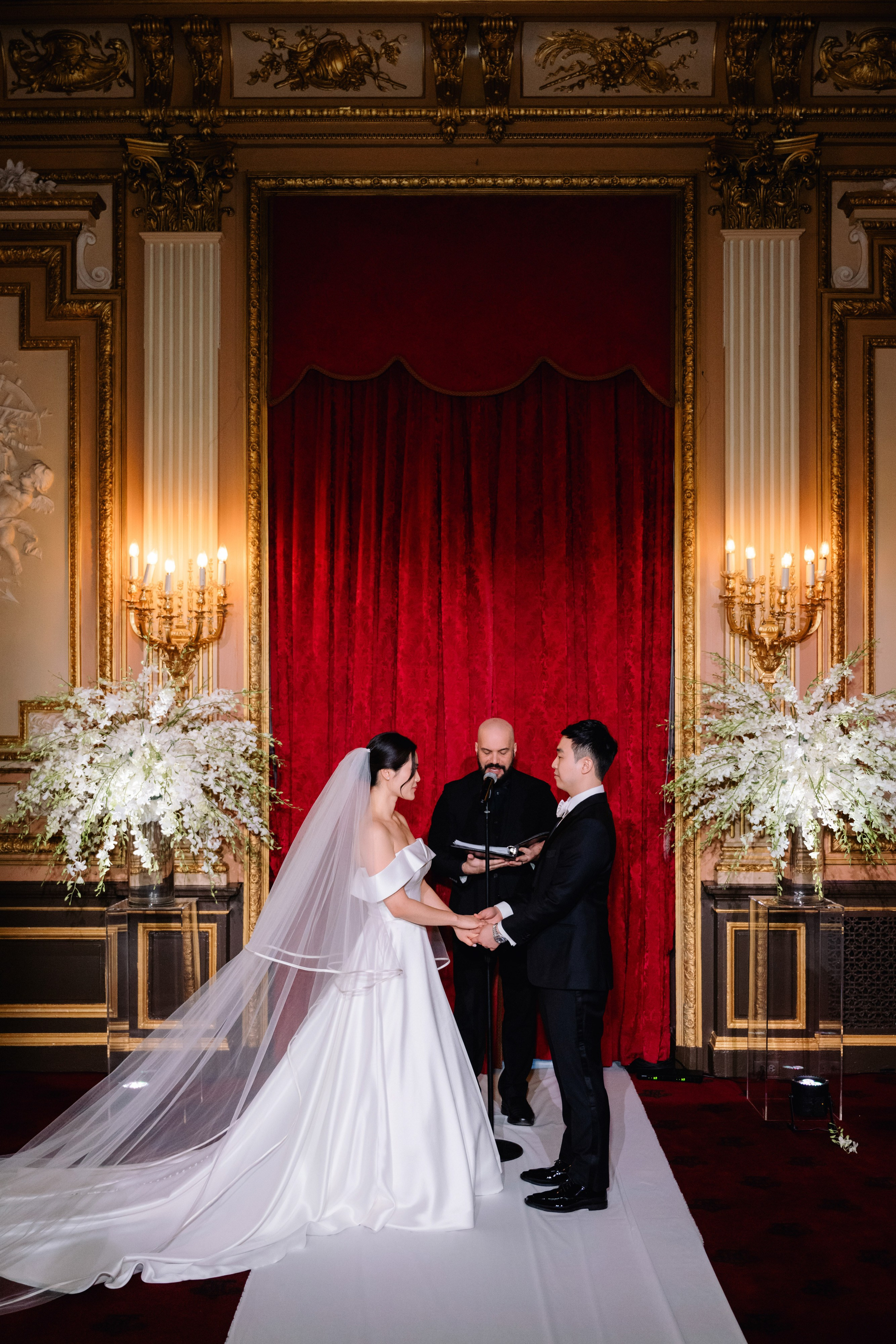 a bride and groom are standing in front of a red curtain