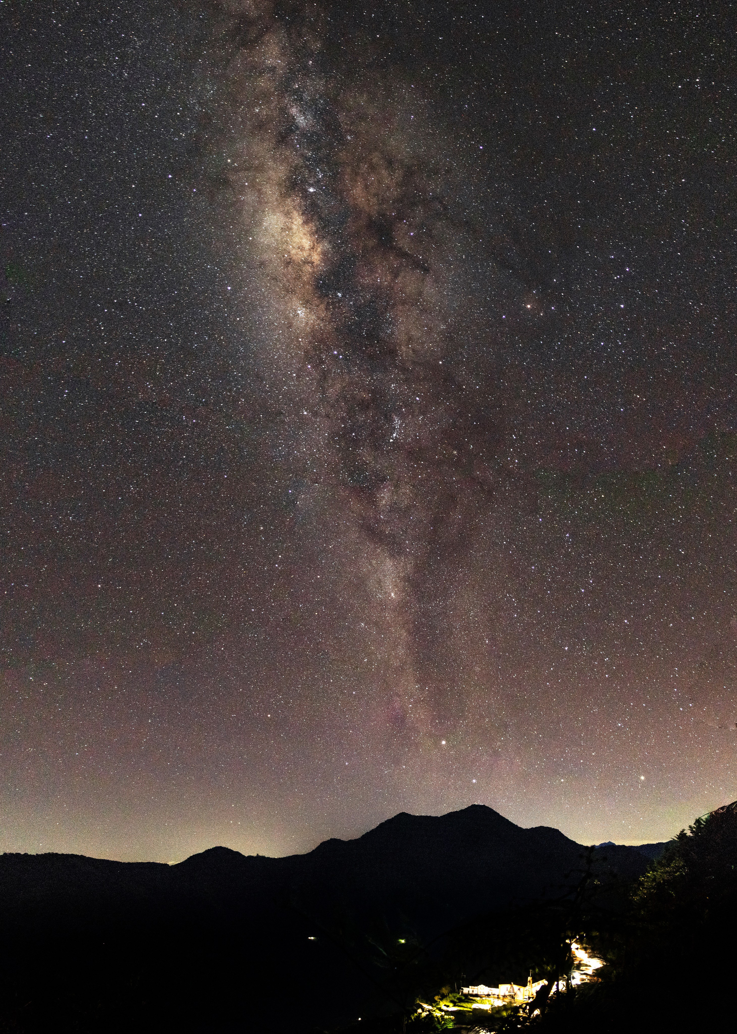 Paisaje de la vía láctea con montañas y un pueblo bajo ella
